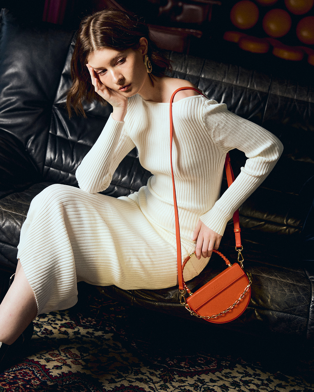 Studio fashion before retouching — cream ribbed dress, orange bag, leather couch
