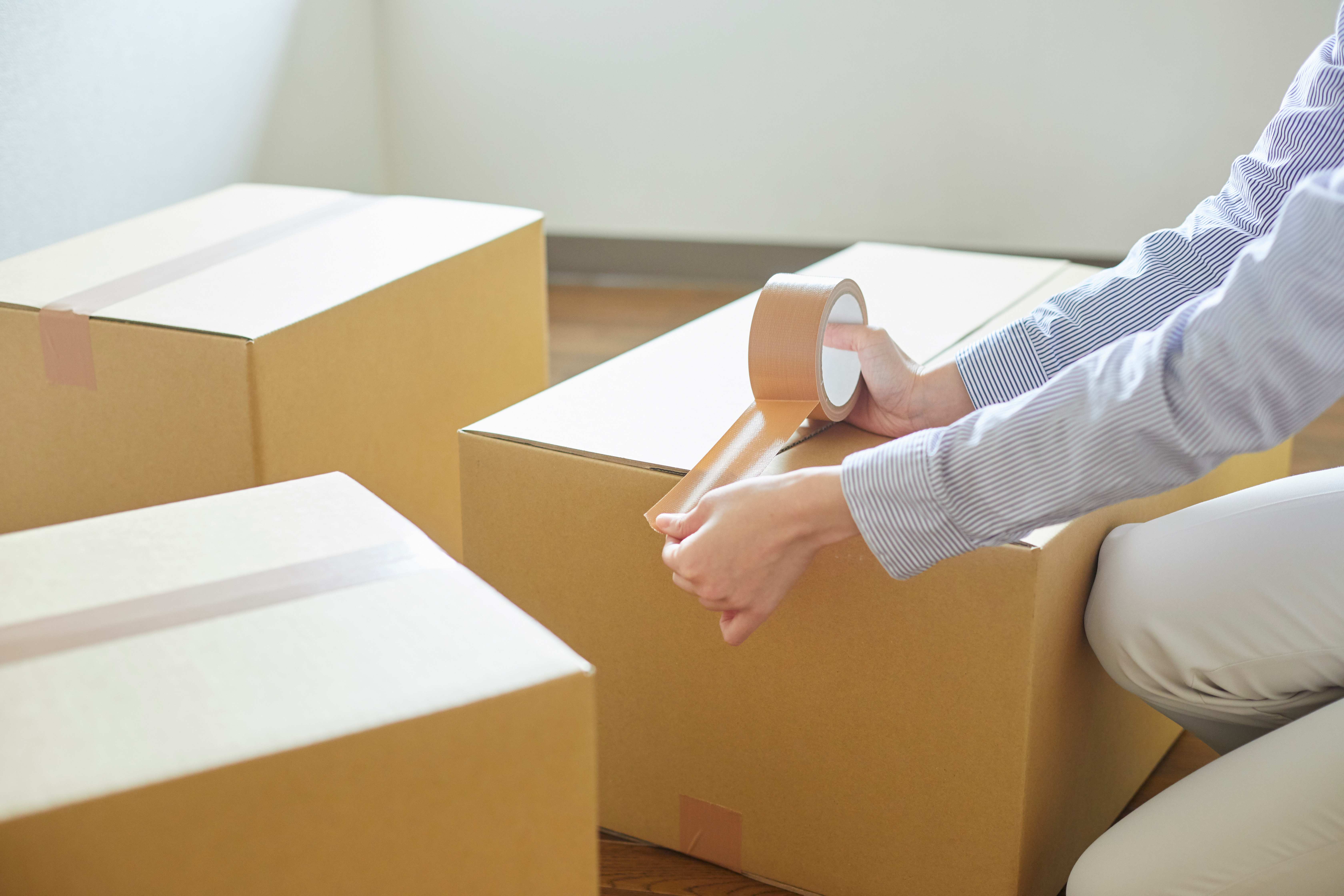 Junge Frau beim Umzug – Packen von Kartons mit Klebeband