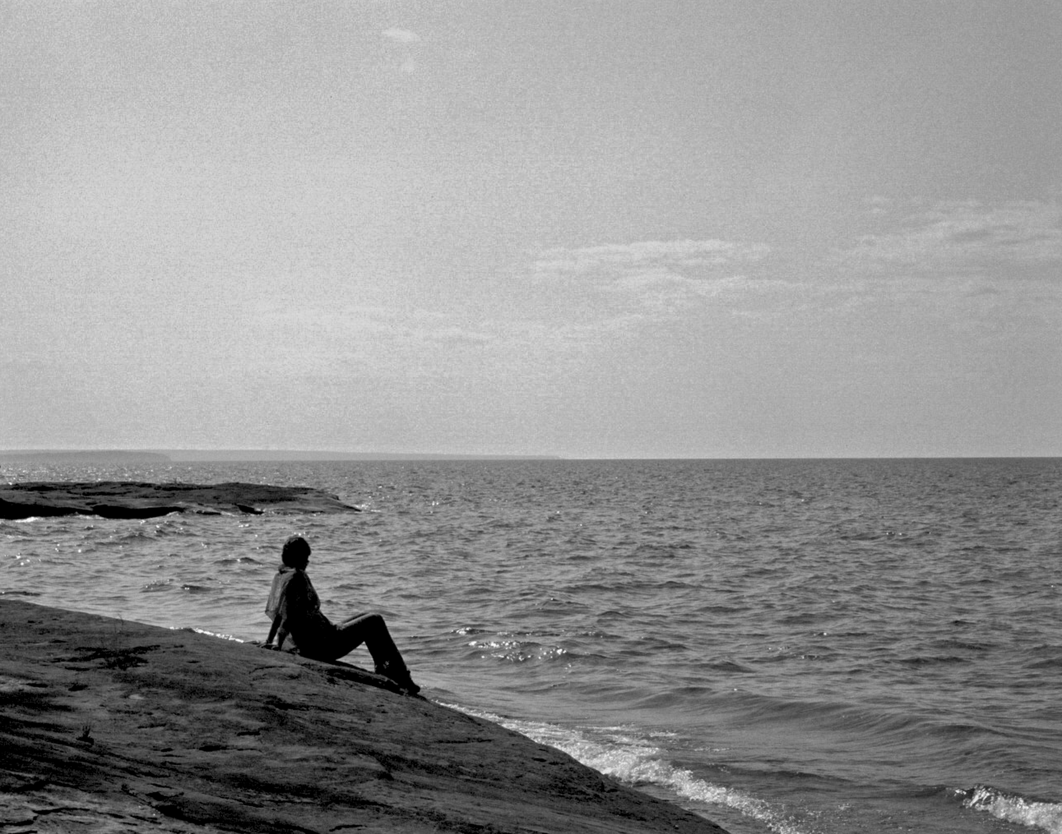 Person sitting alone on rocky shoreline gazing out over vast Lake Superior waters