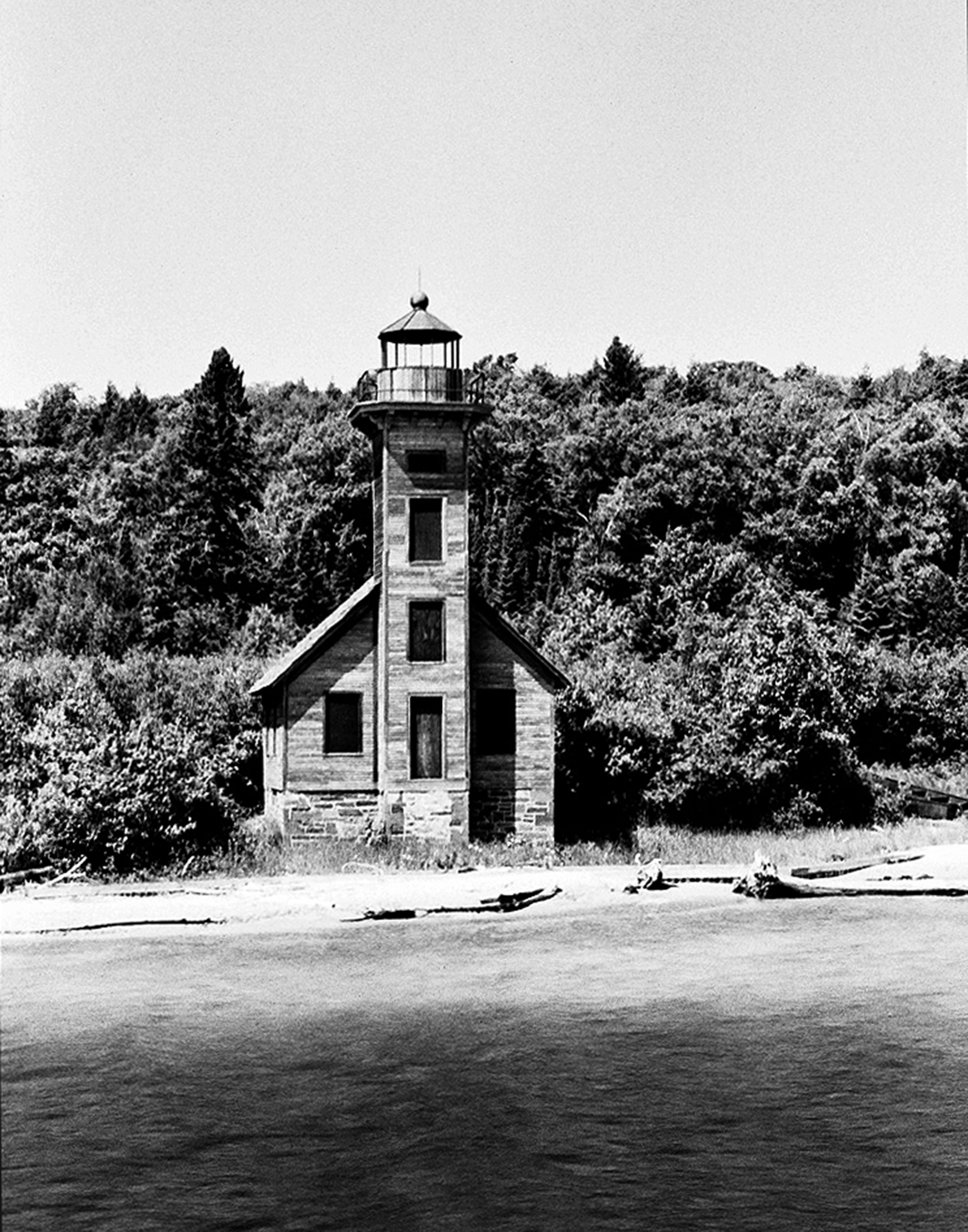 Historic wooden lighthouse with tower on Lake Superior shoreline surrounded by dense forest