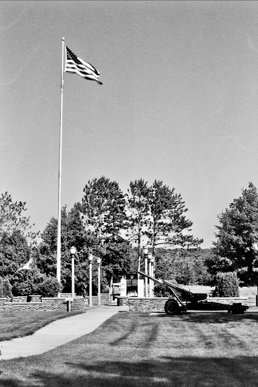 American flag flying on tall pole at veterans memorial with artillery cannon and lamp posts