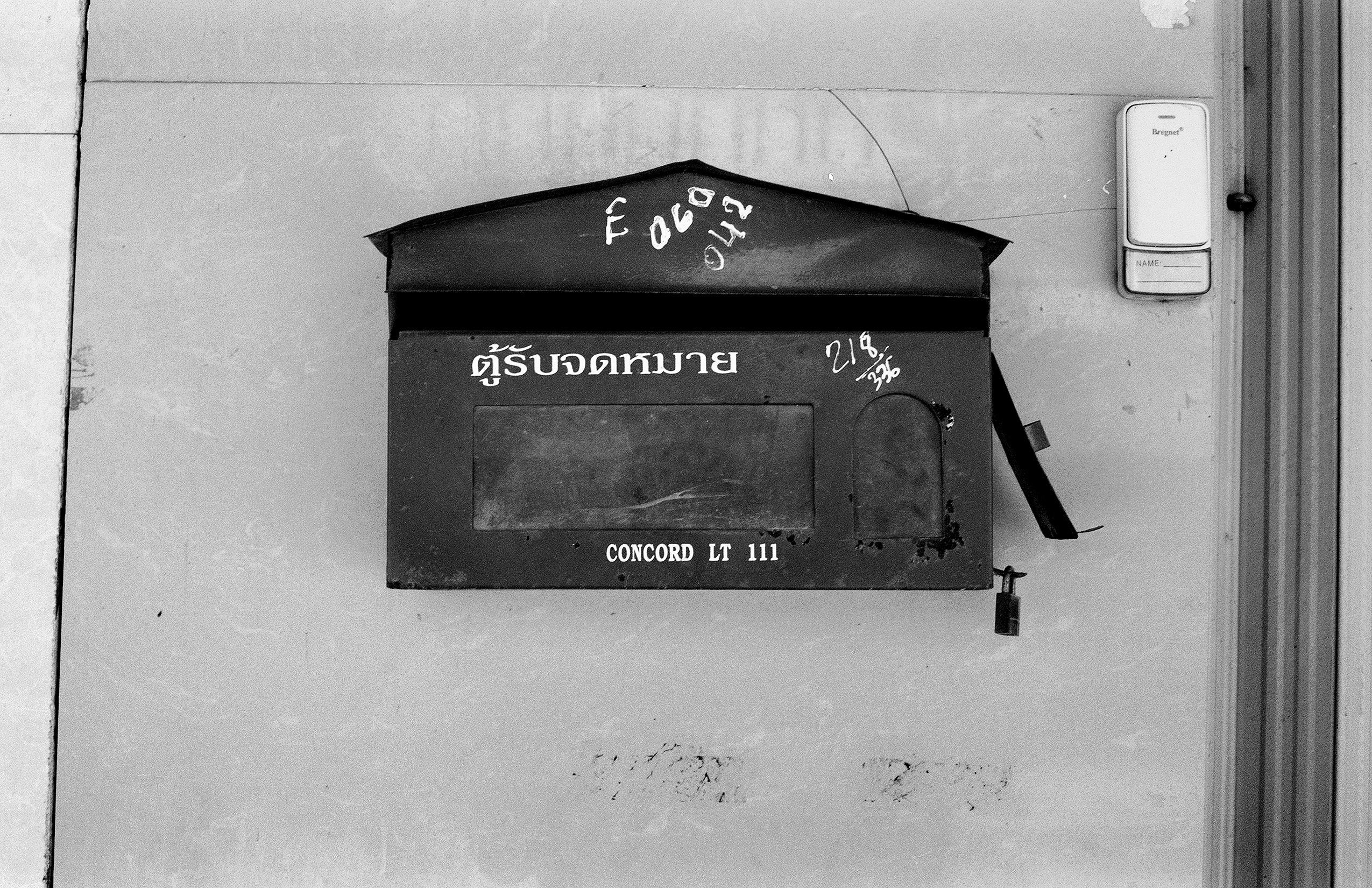 Black mailbox with Thai text and handwritten markings on white concrete wall