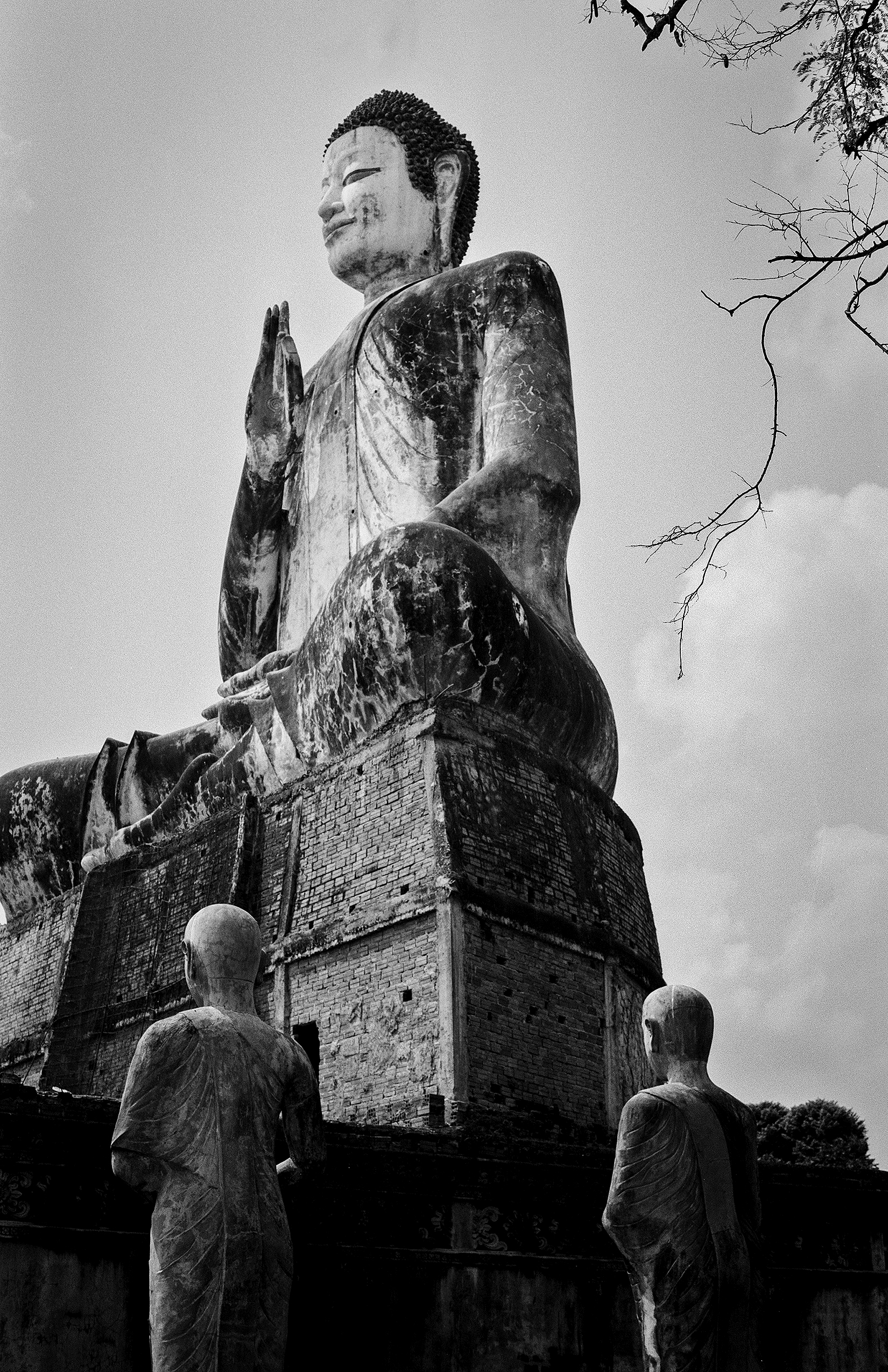 Large Buddha statue in meditation pose with protective monk figures standing below