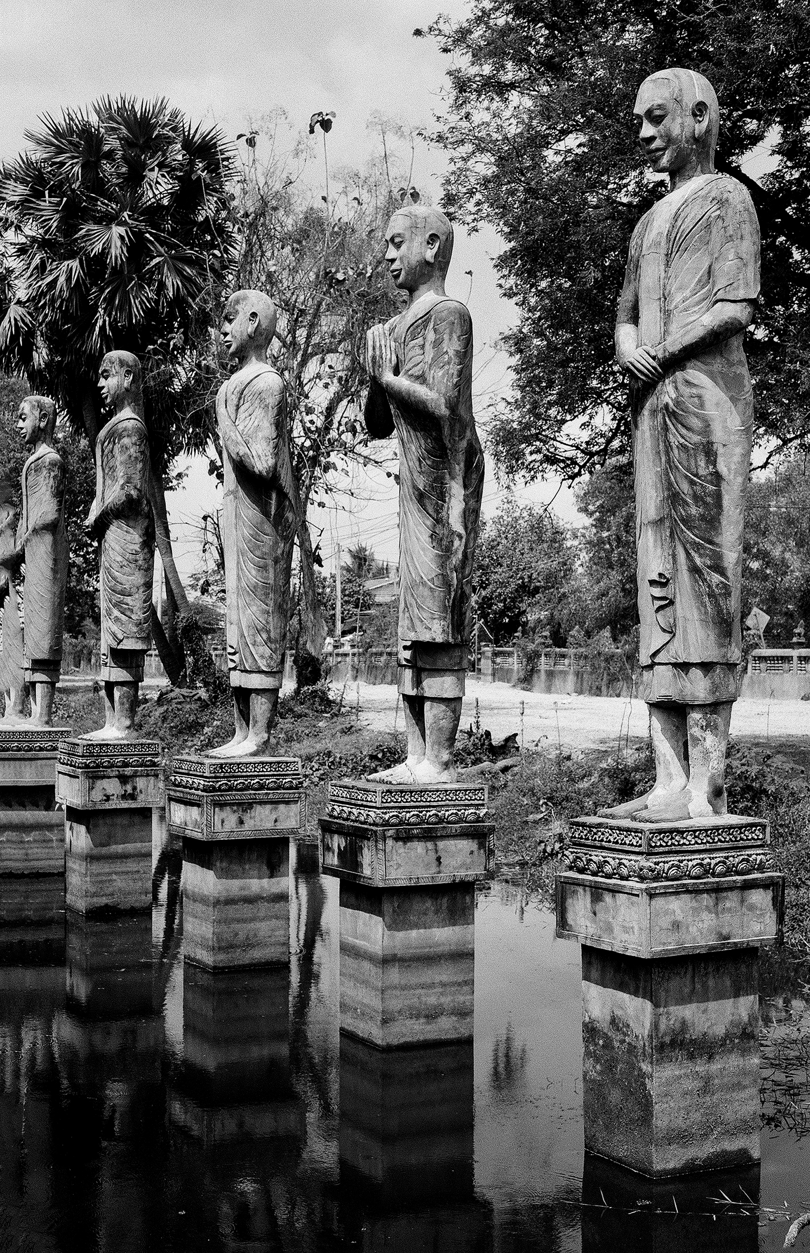 Multiple wooden monk statues in traditional robes standing on pedestals in flooded temple ground
