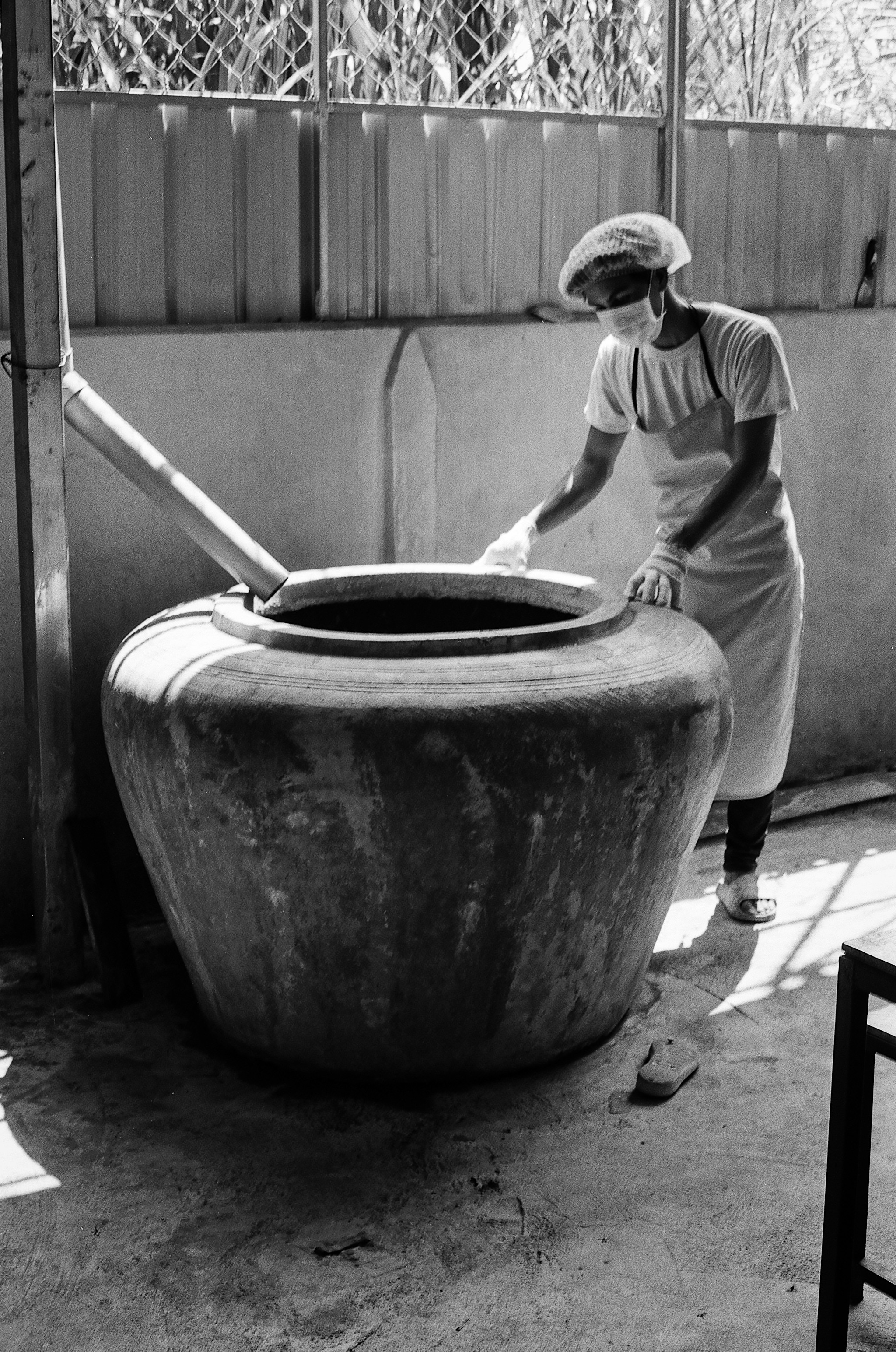 Woman in white shirt working with large round ceramic water vessel in courtyard