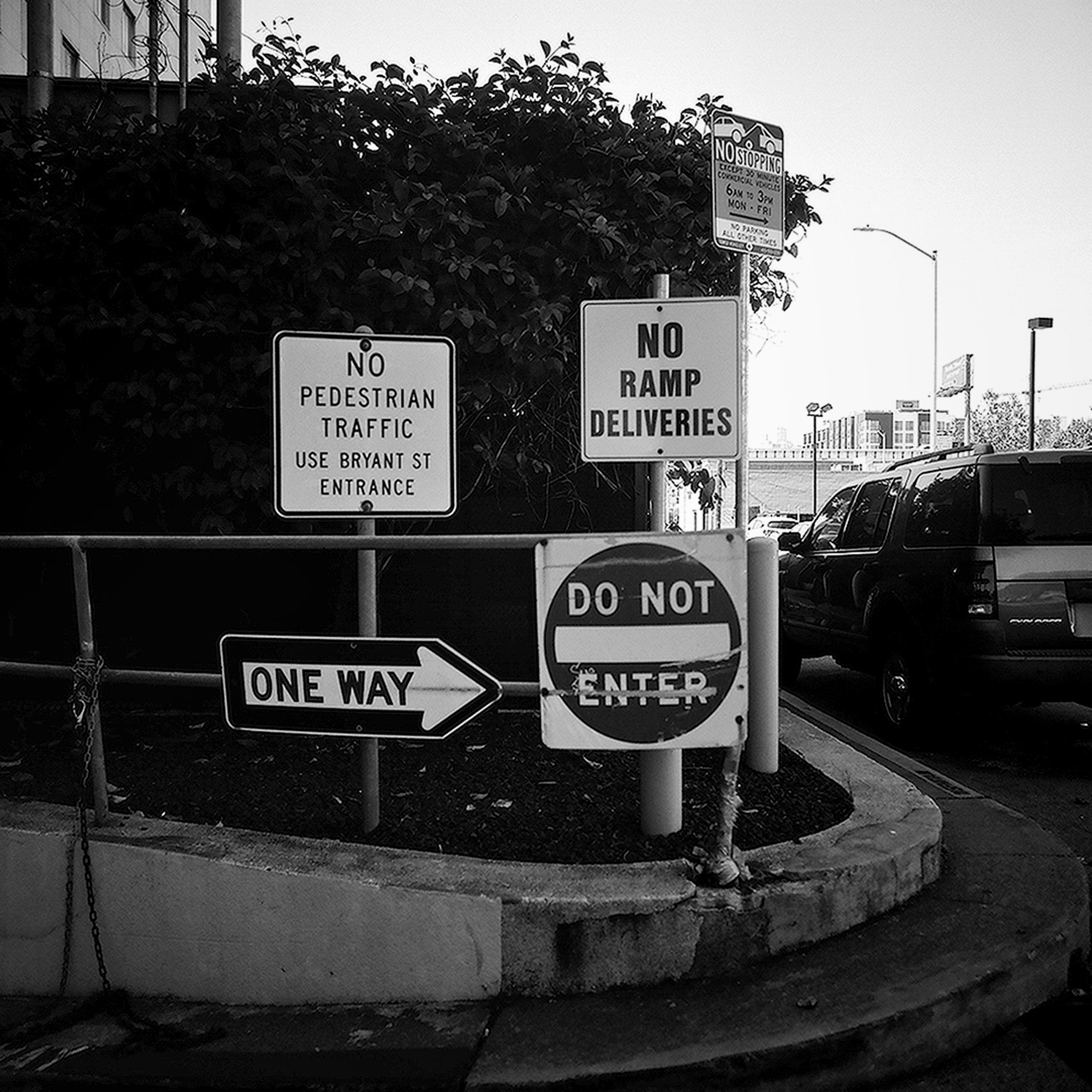 Urban intersection with multiple street signs No Pedestrian Traffic One Way Do Not Enter parked vehicles in background