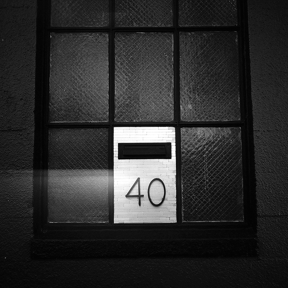 Industrial window with wire glass panes and number 40 visible on white brick wall through frame
