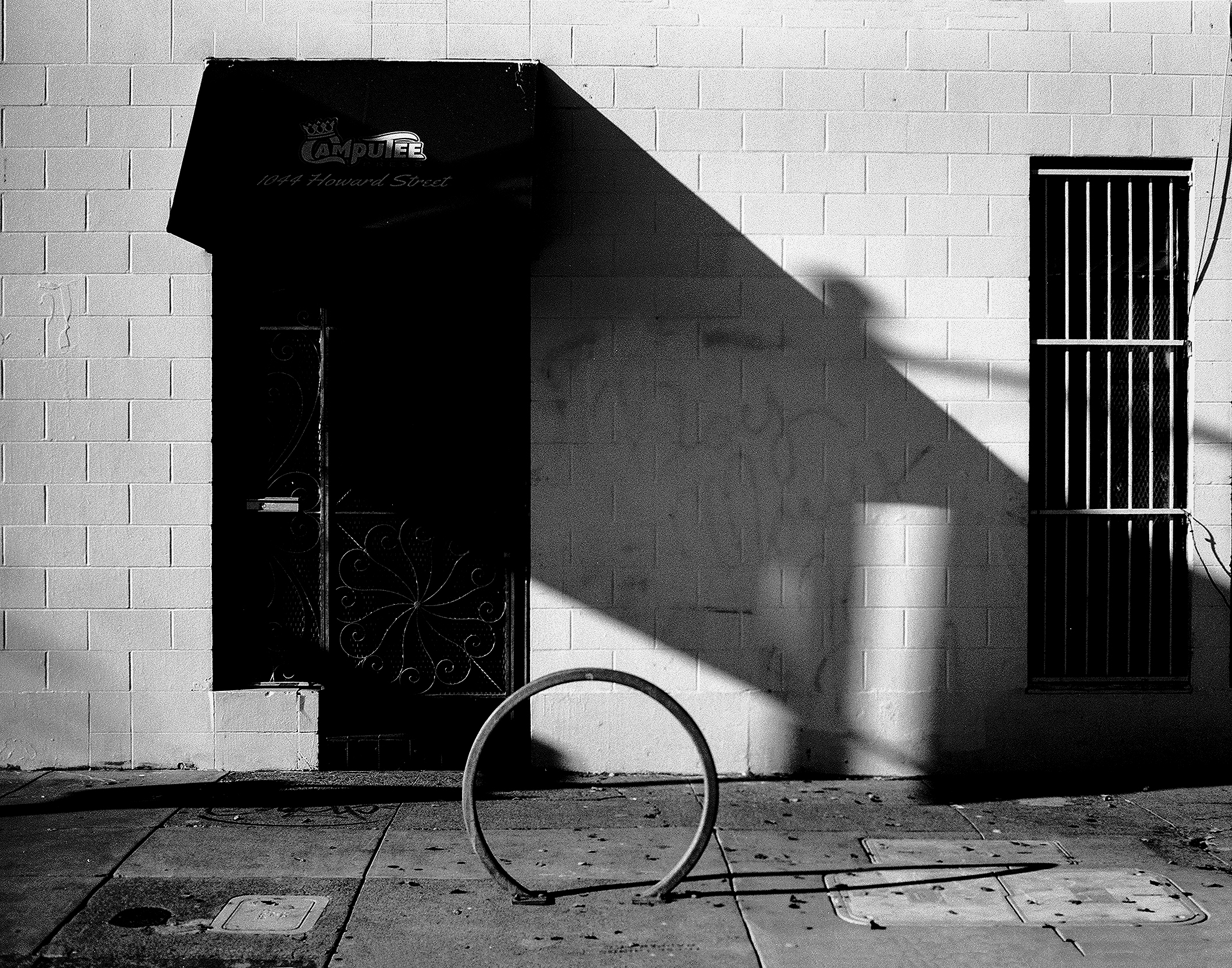 Howard Street storefront with Campsite awning casting dramatic shadow on white brick wall and circular bike rack on sidewalk