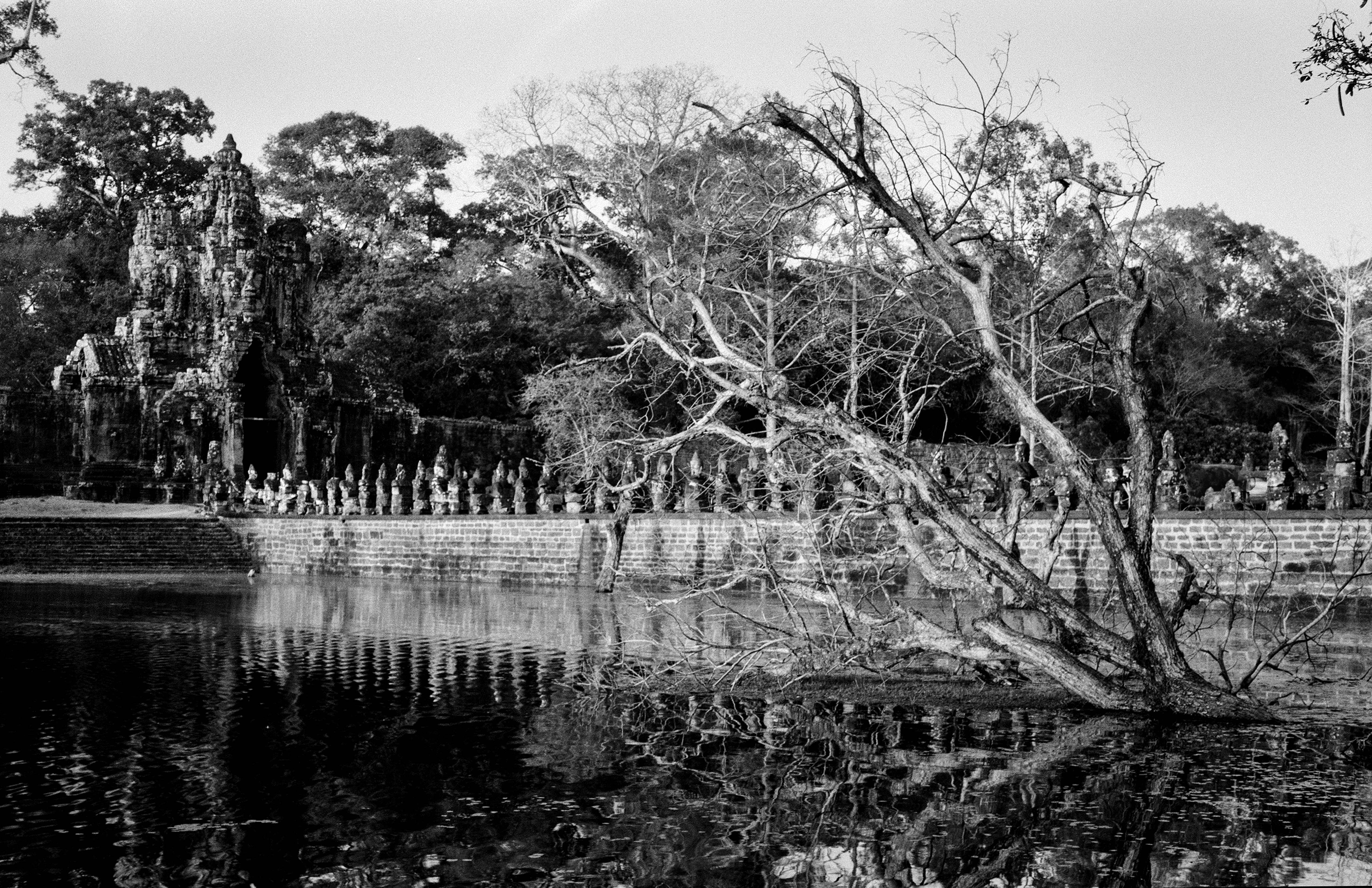 Ancient temple ruins partially submerged in water with stone sculptures and trees