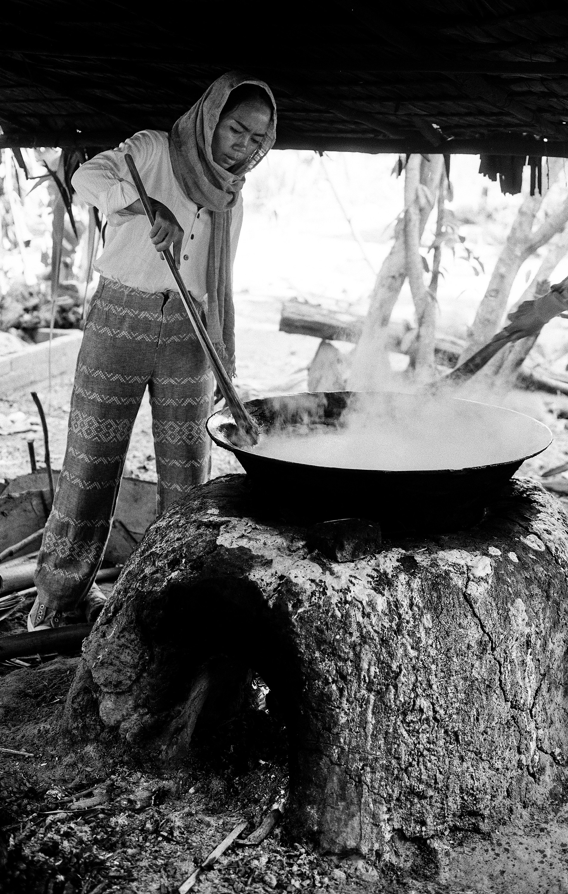 Woman stirring large metal wok over open fire with traditional cooking technique