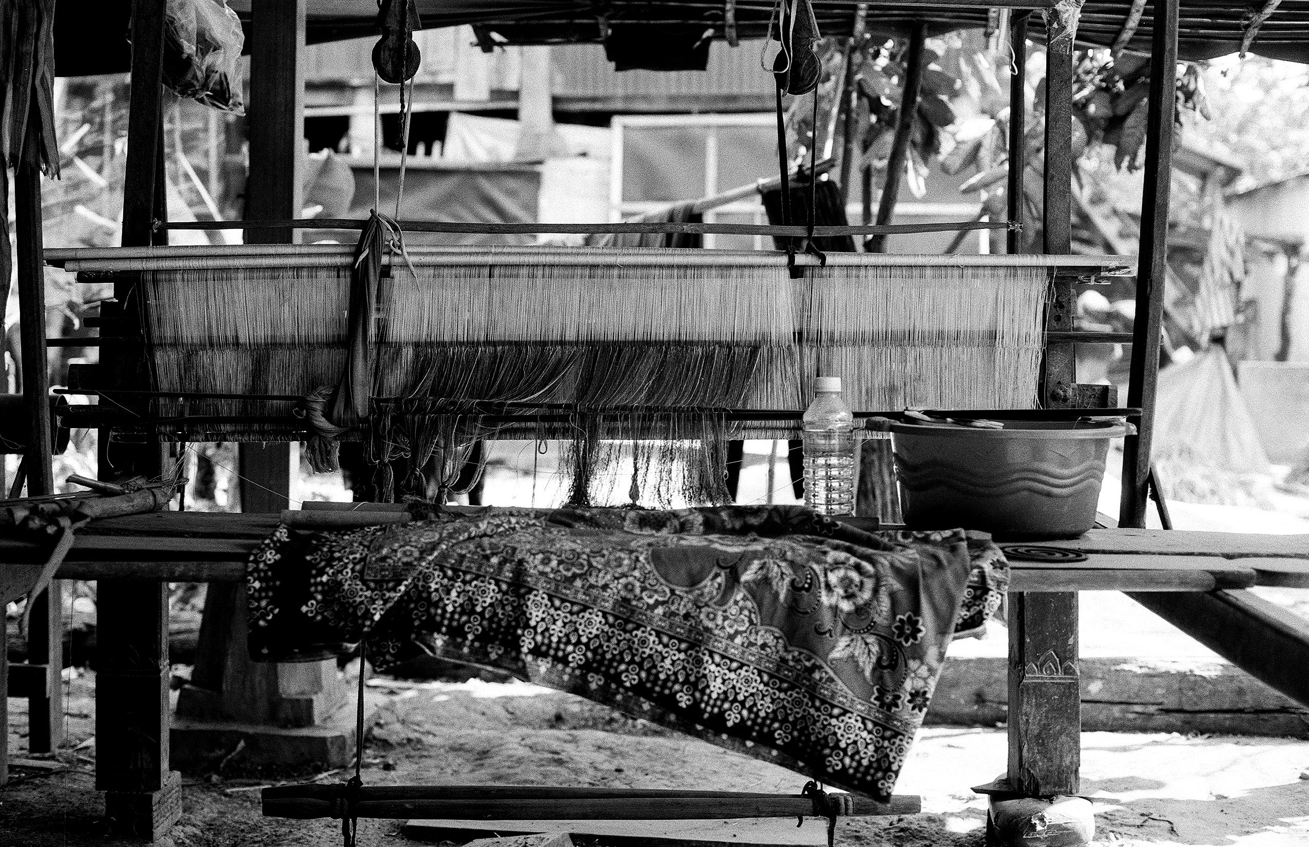 Woman operating traditional hand loom with white silk threads and pulleys