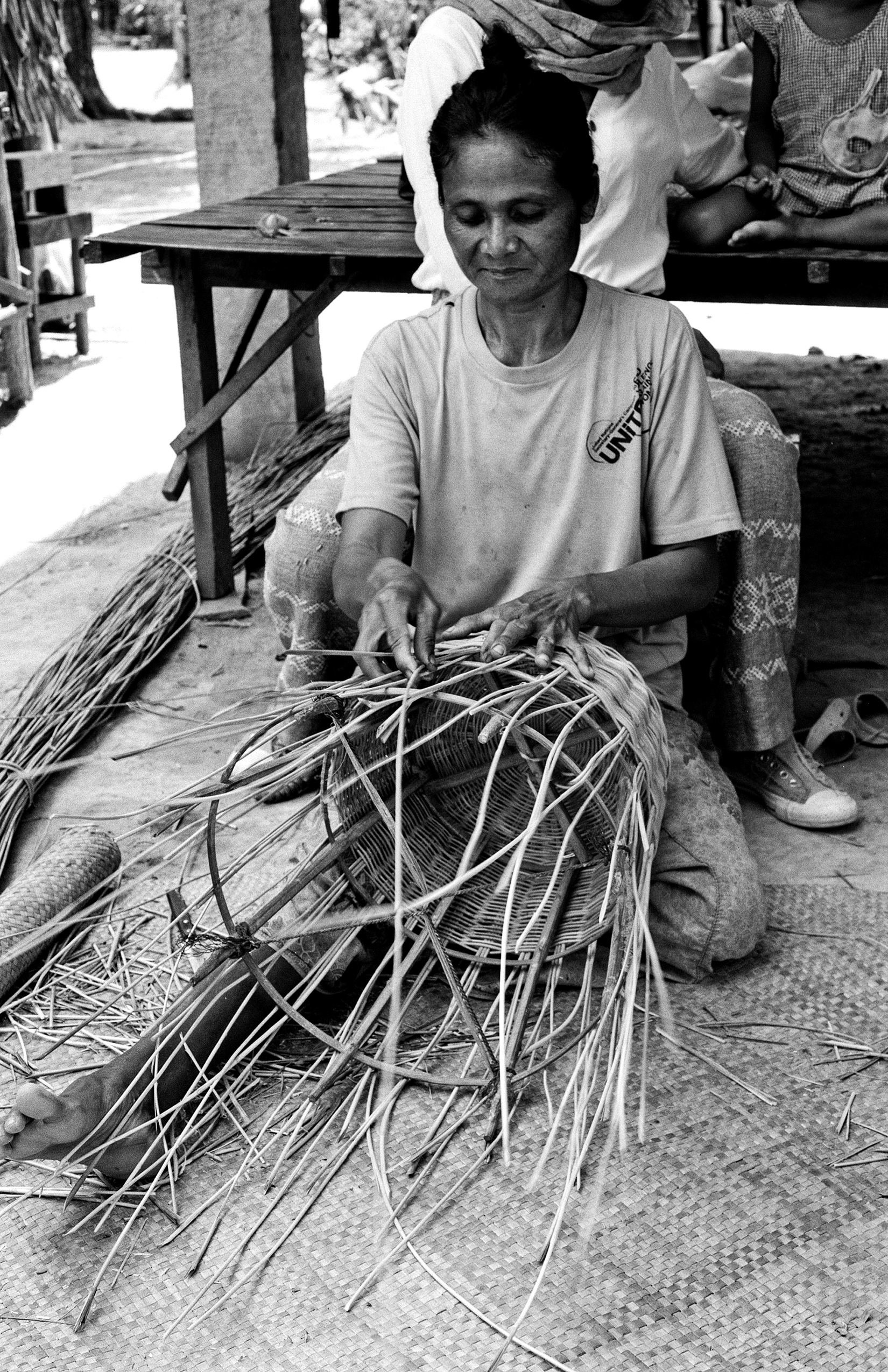 Woman sitting weaving strips of palm or rattan material with practiced hands