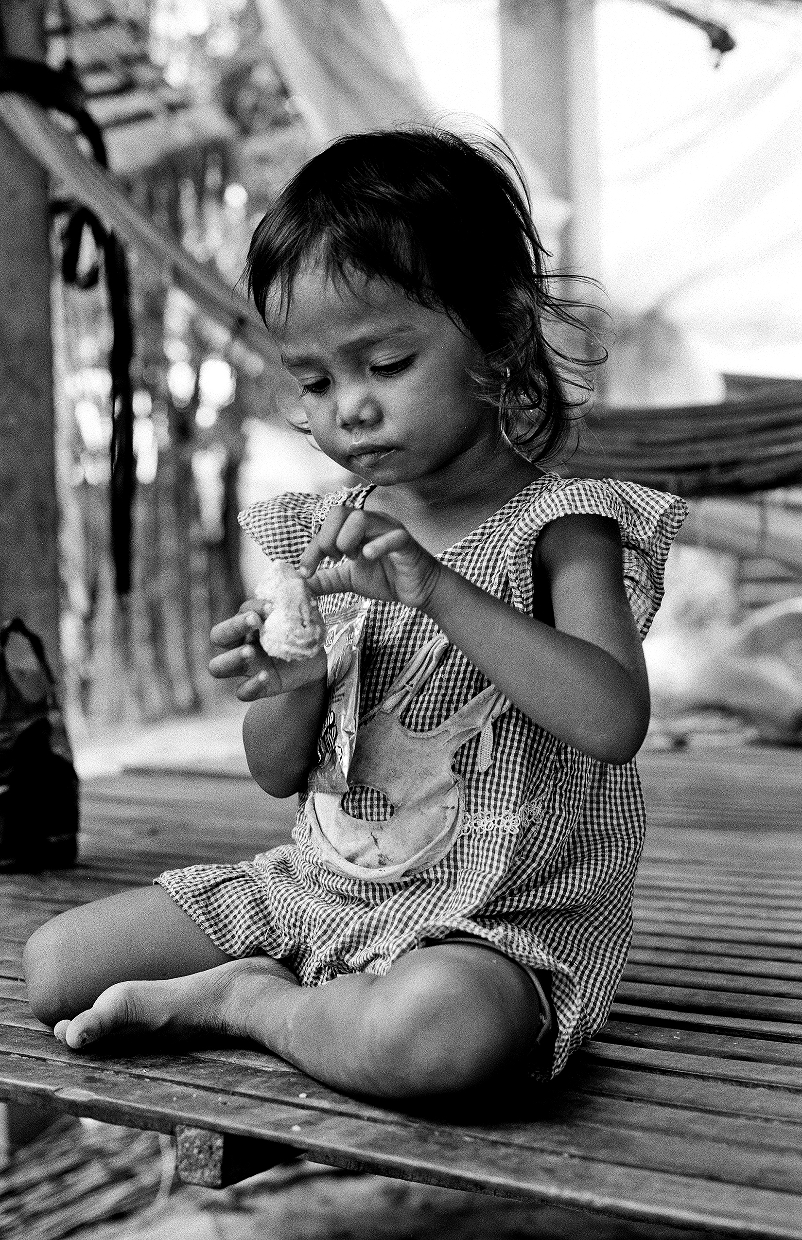 Small Cambodian child in checkered shirt sitting and looking downward