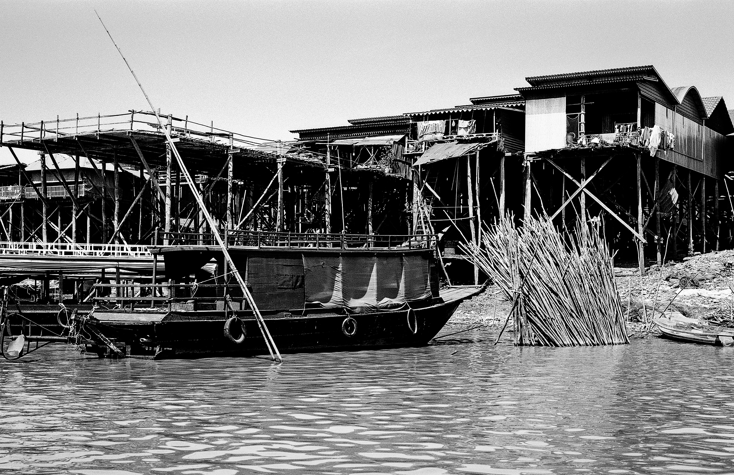 Wooden stilt houses on riverbank with boats moored and mangrove forest behind