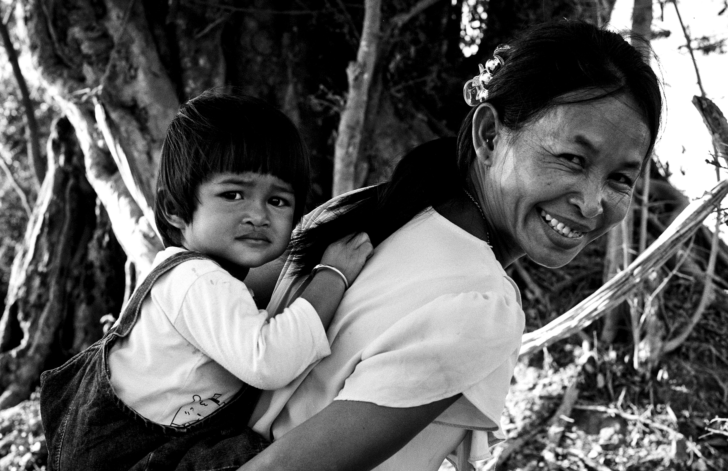 Smiling mother carrying young child on her back in forest with foliage