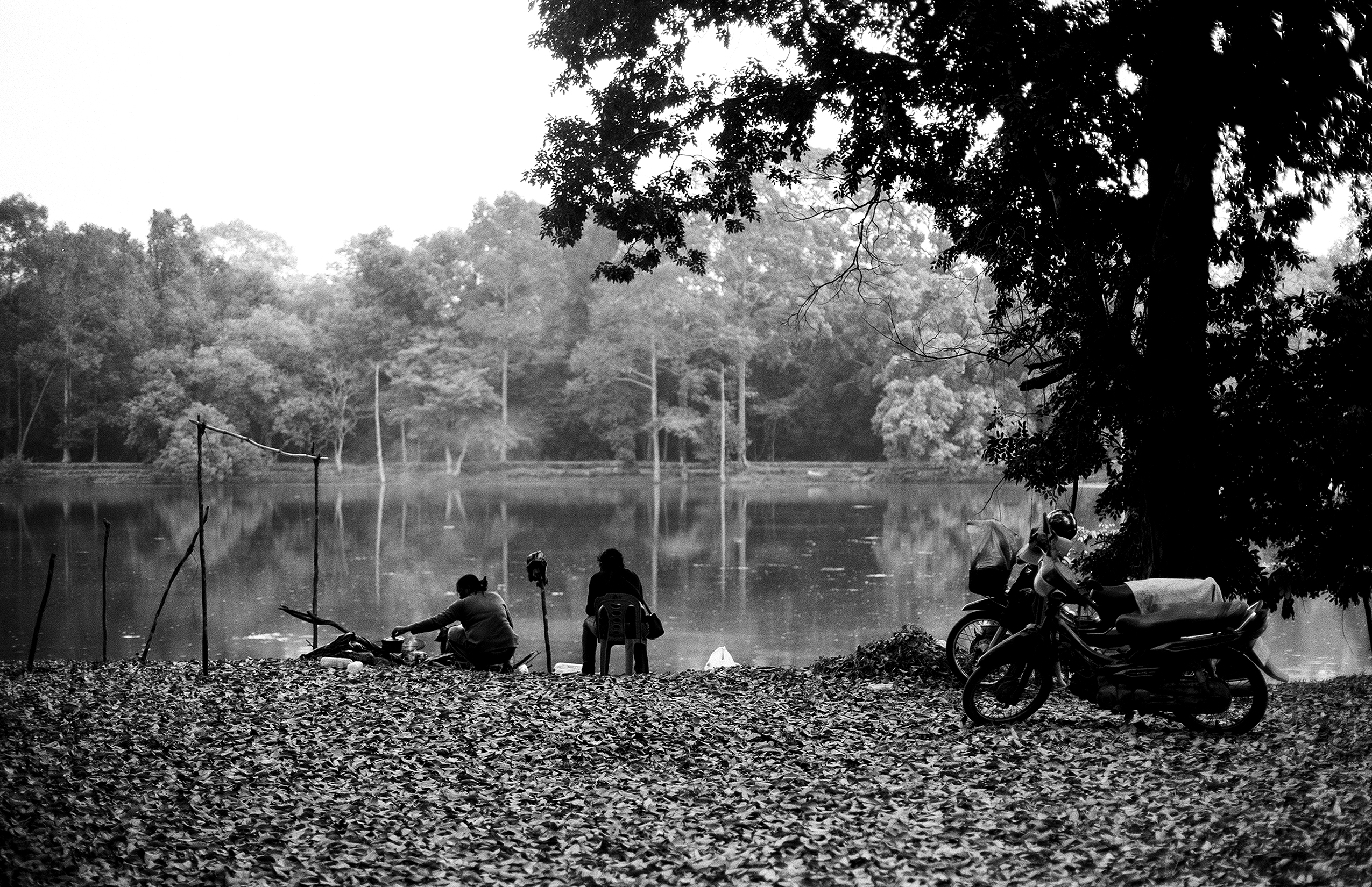 Riverside scene with motorcycle parked near fishermen and wooden boat at dusk