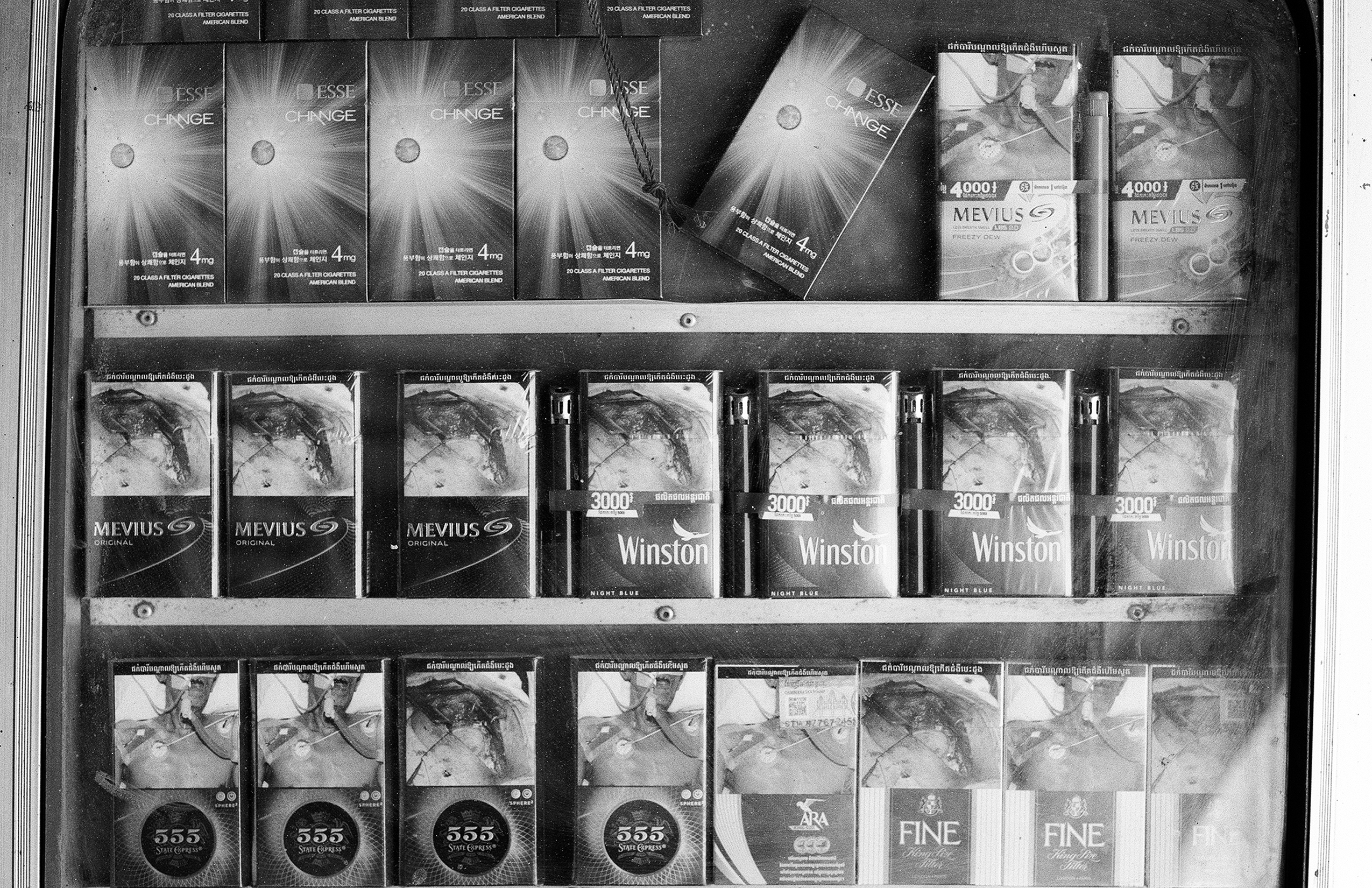 Store shelves displaying various cigarette brands with Khmer script text labels