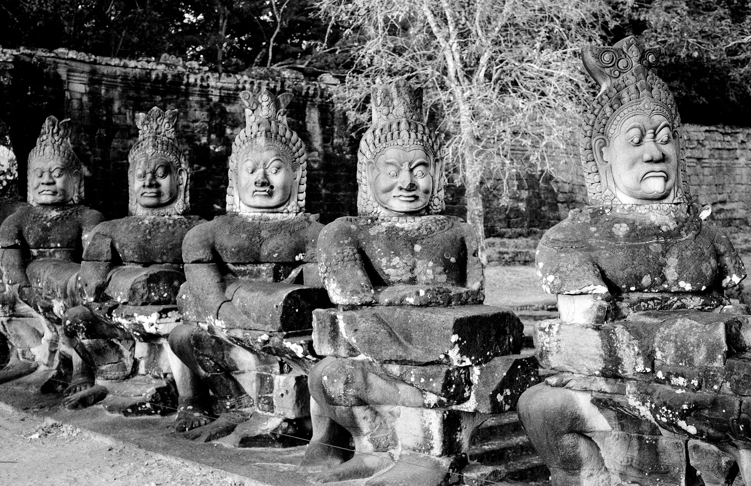 Row of five stone guardian statues with elaborate headdresses weathered by time