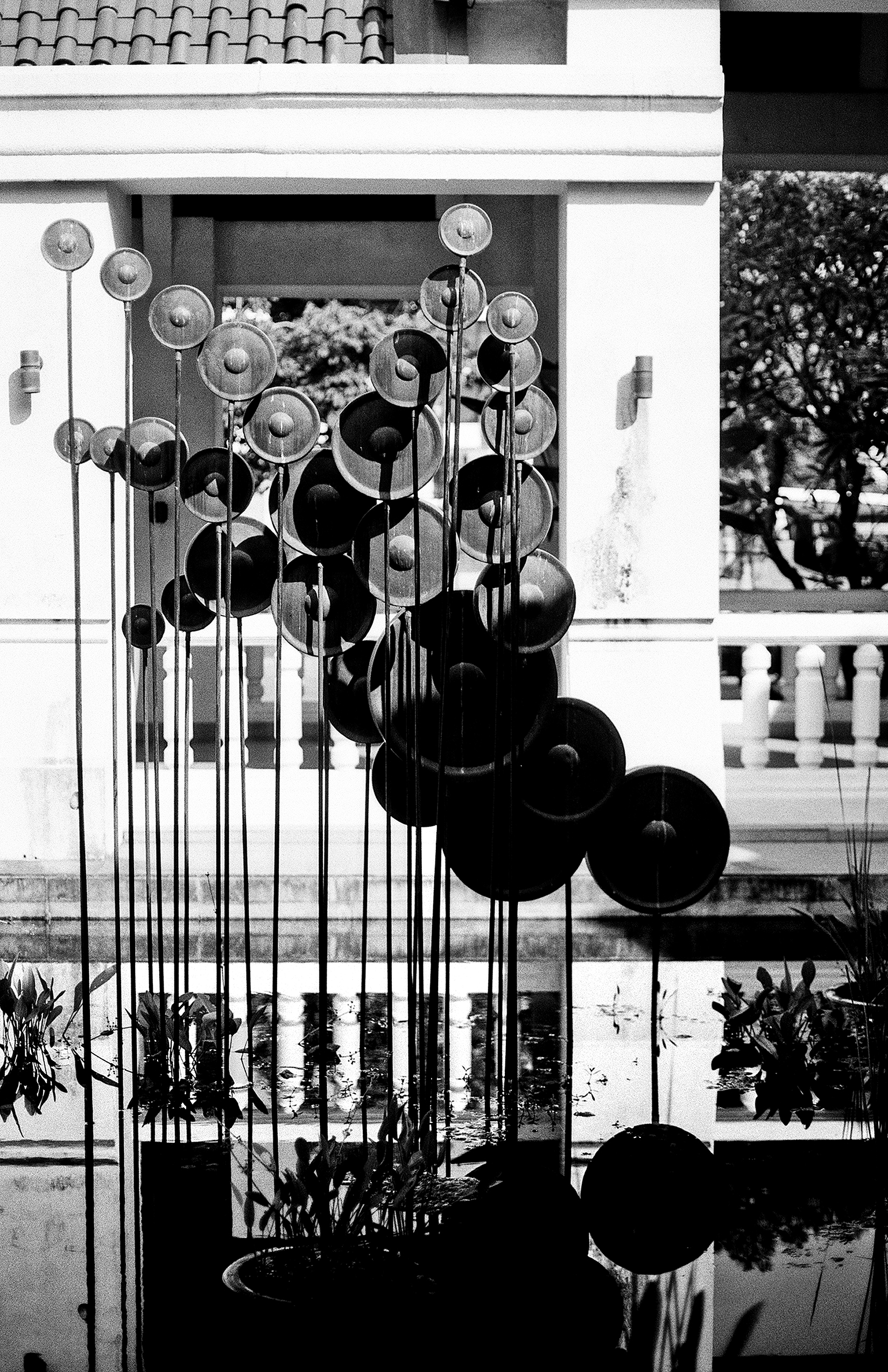 Metal wind chime sculpture with hanging discs on classical colonnade with reflection