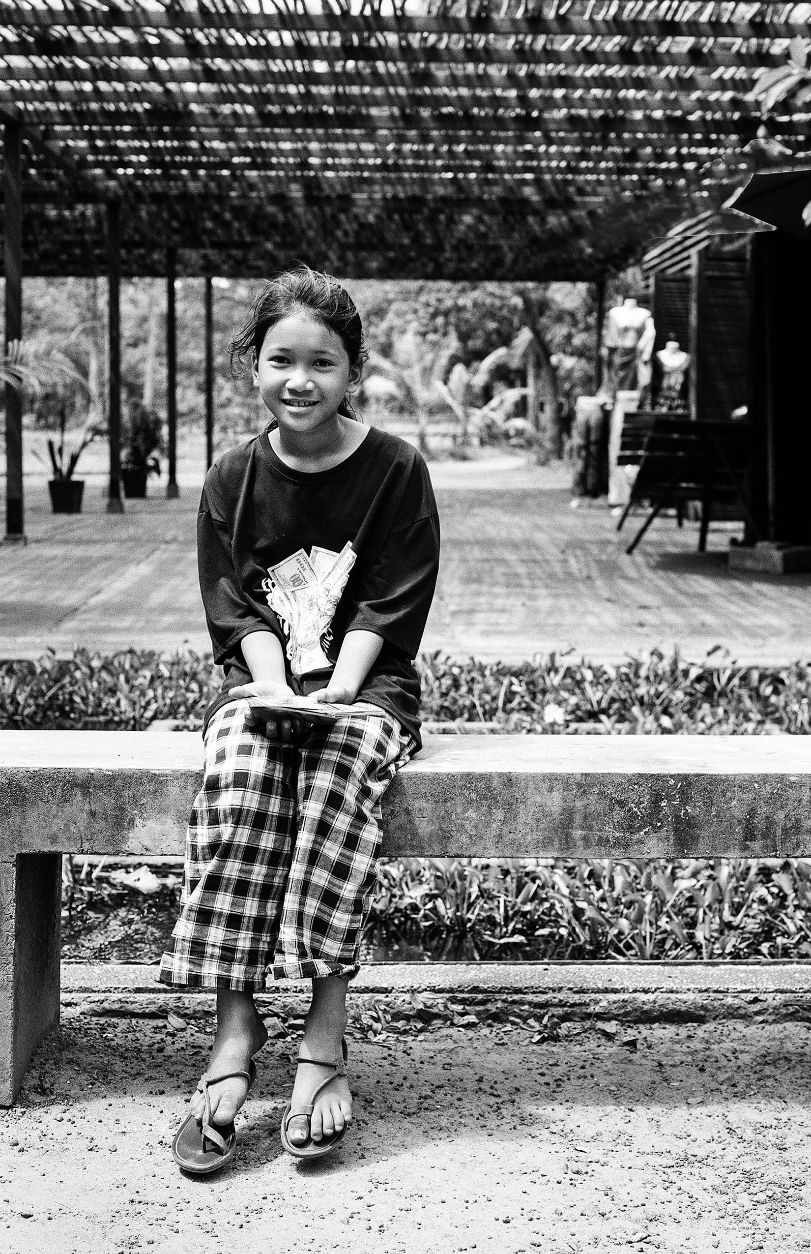 Woman shoe vendor smiling while sitting surrounded by various sandals and footwear display