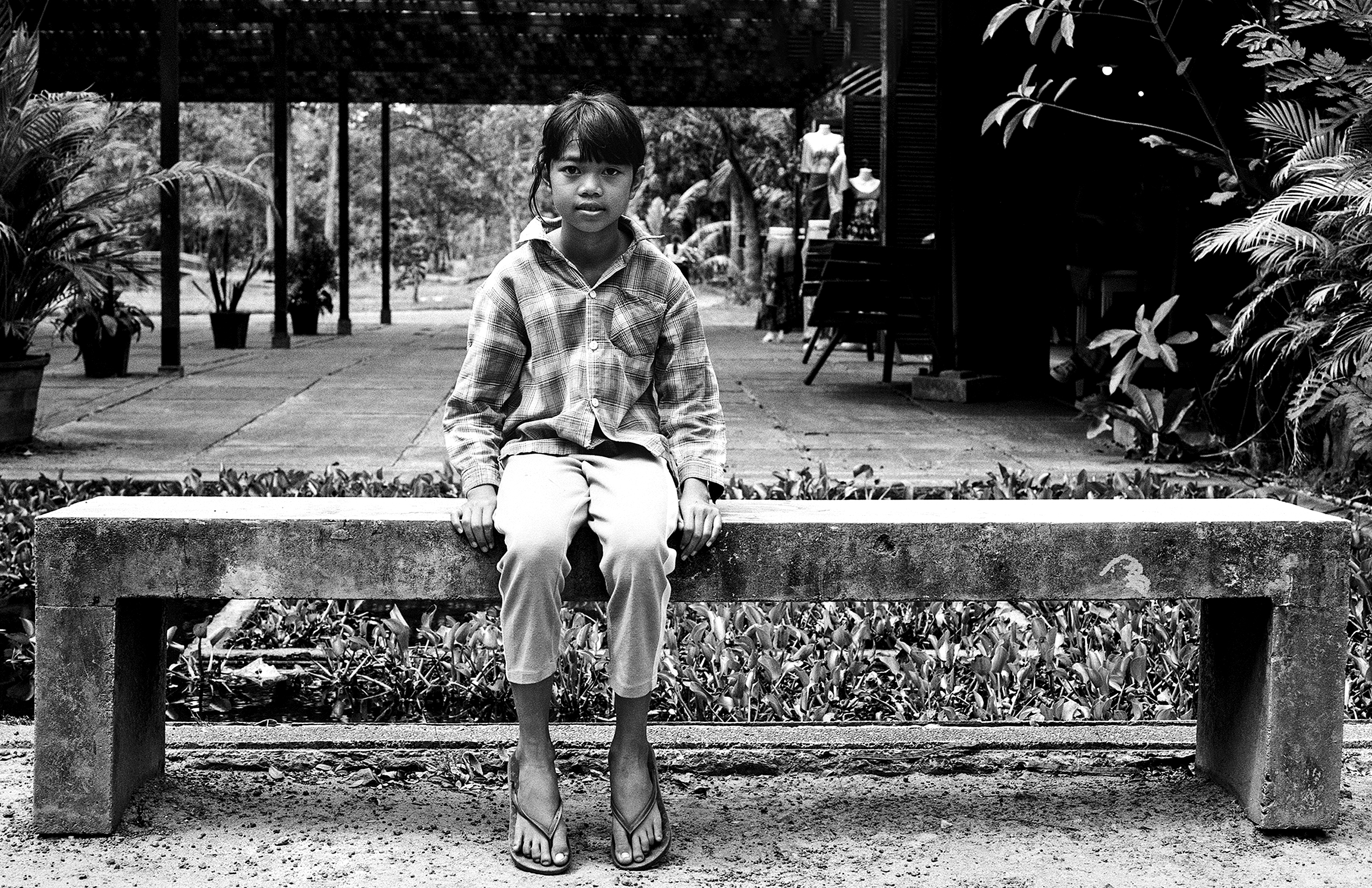 Child sitting on concrete bench surrounded by lush vegetation and potted plants