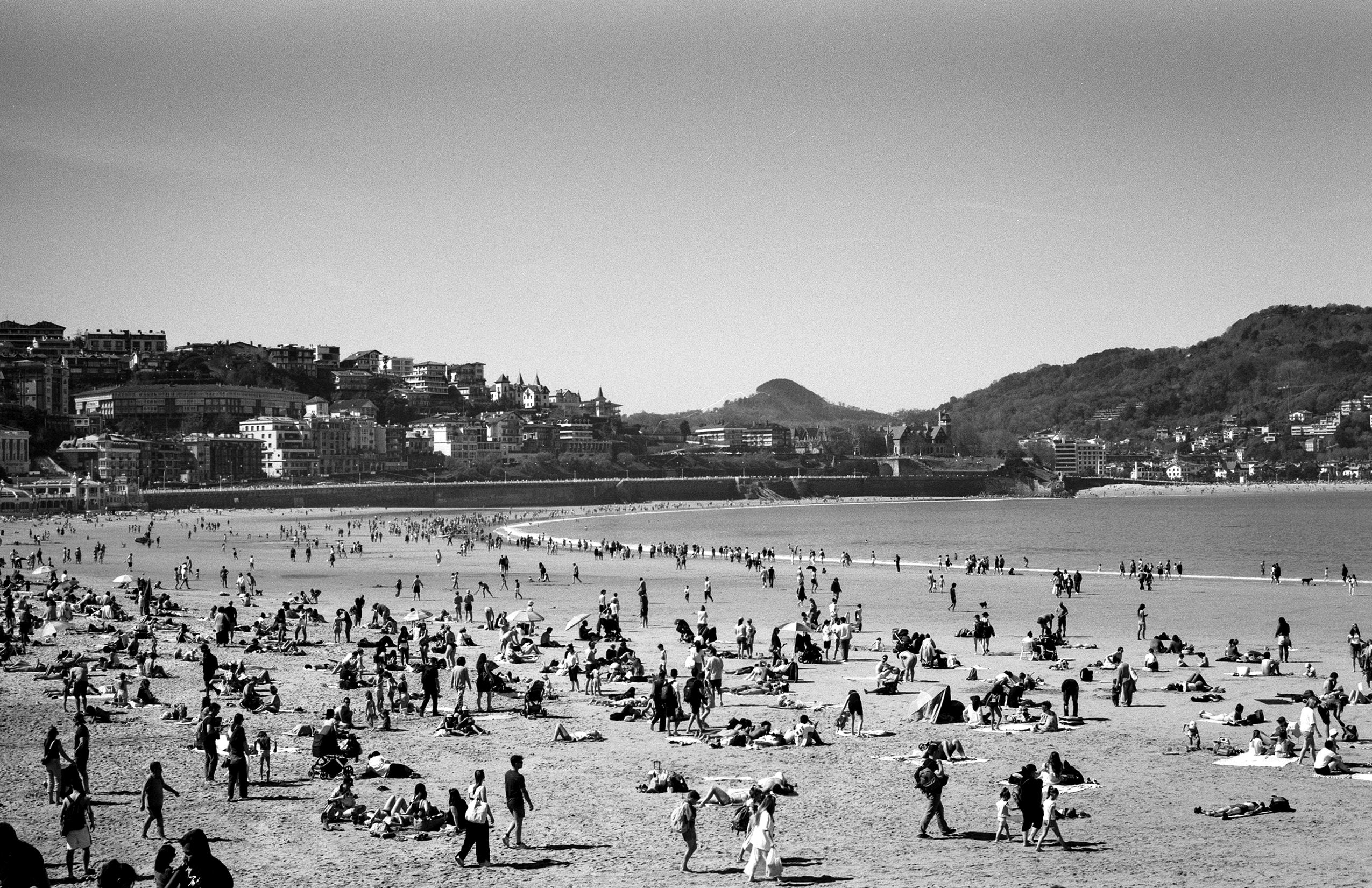Beach crowded with people and umbrellas with coastal town backdrop
