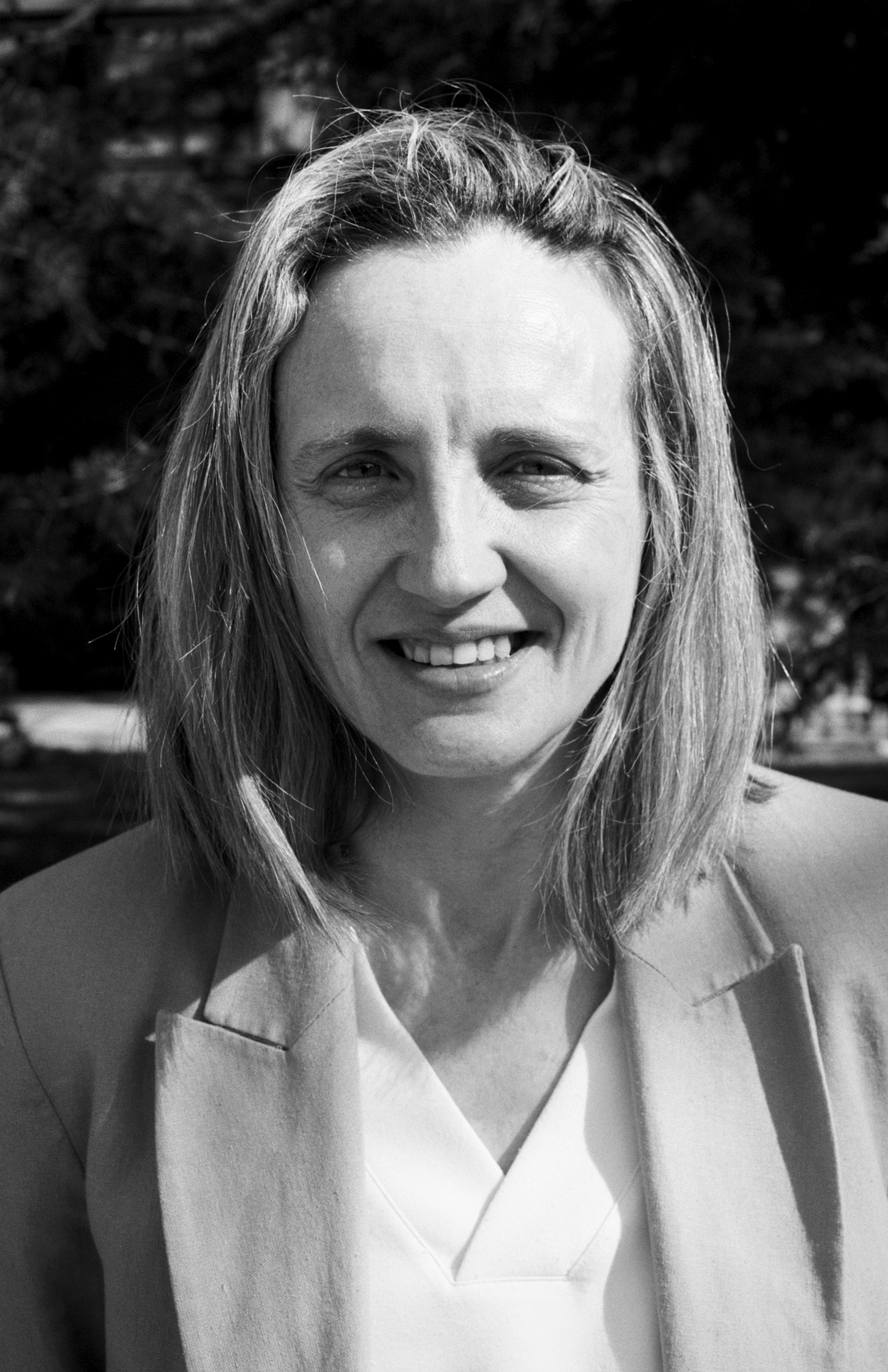 Portrait of woman with long hair smiling at camera wearing light colored jacket outdoors