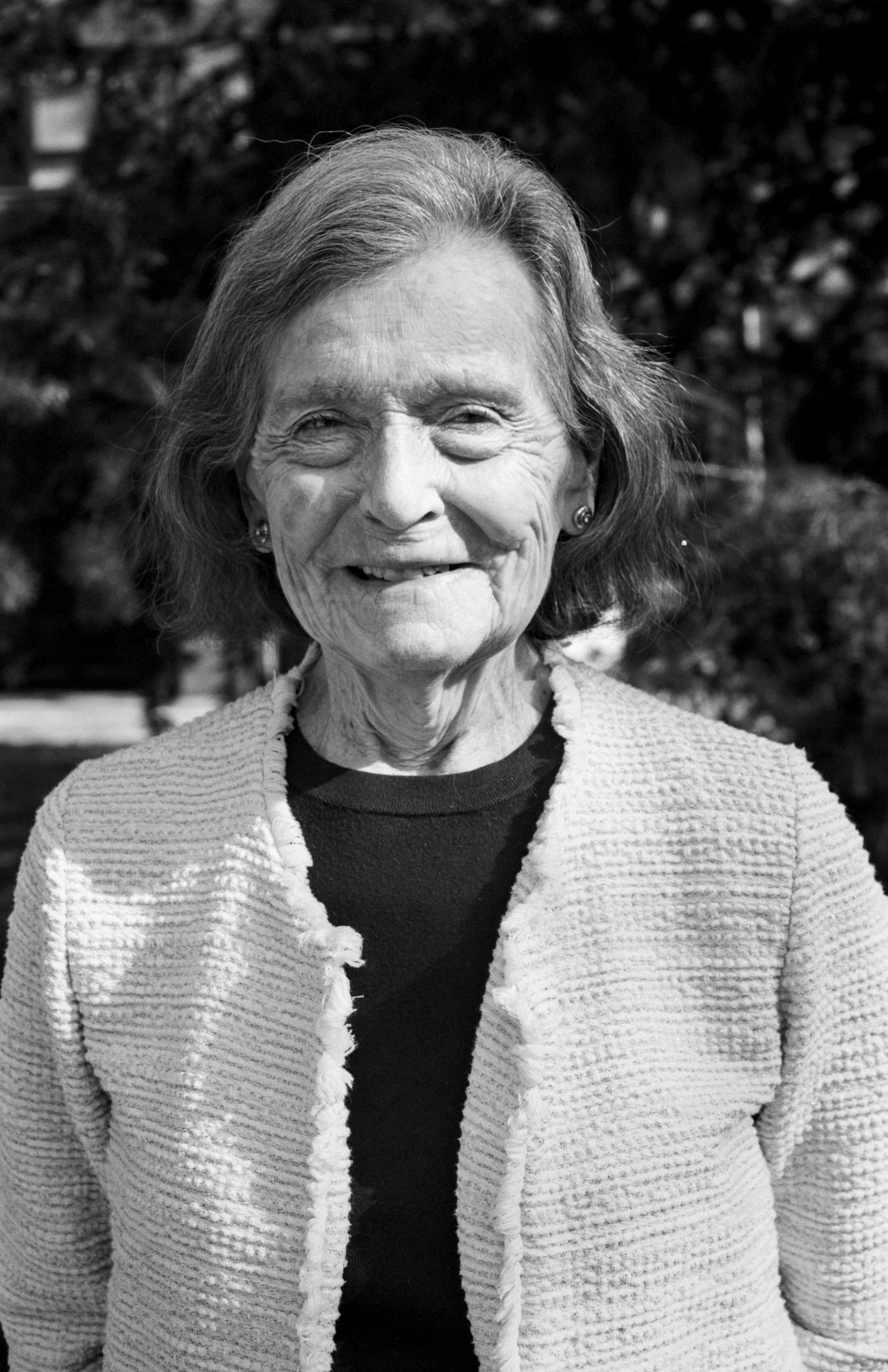 Portrait of elderly woman smiling at camera wearing textured cardigan outdoors in natural light