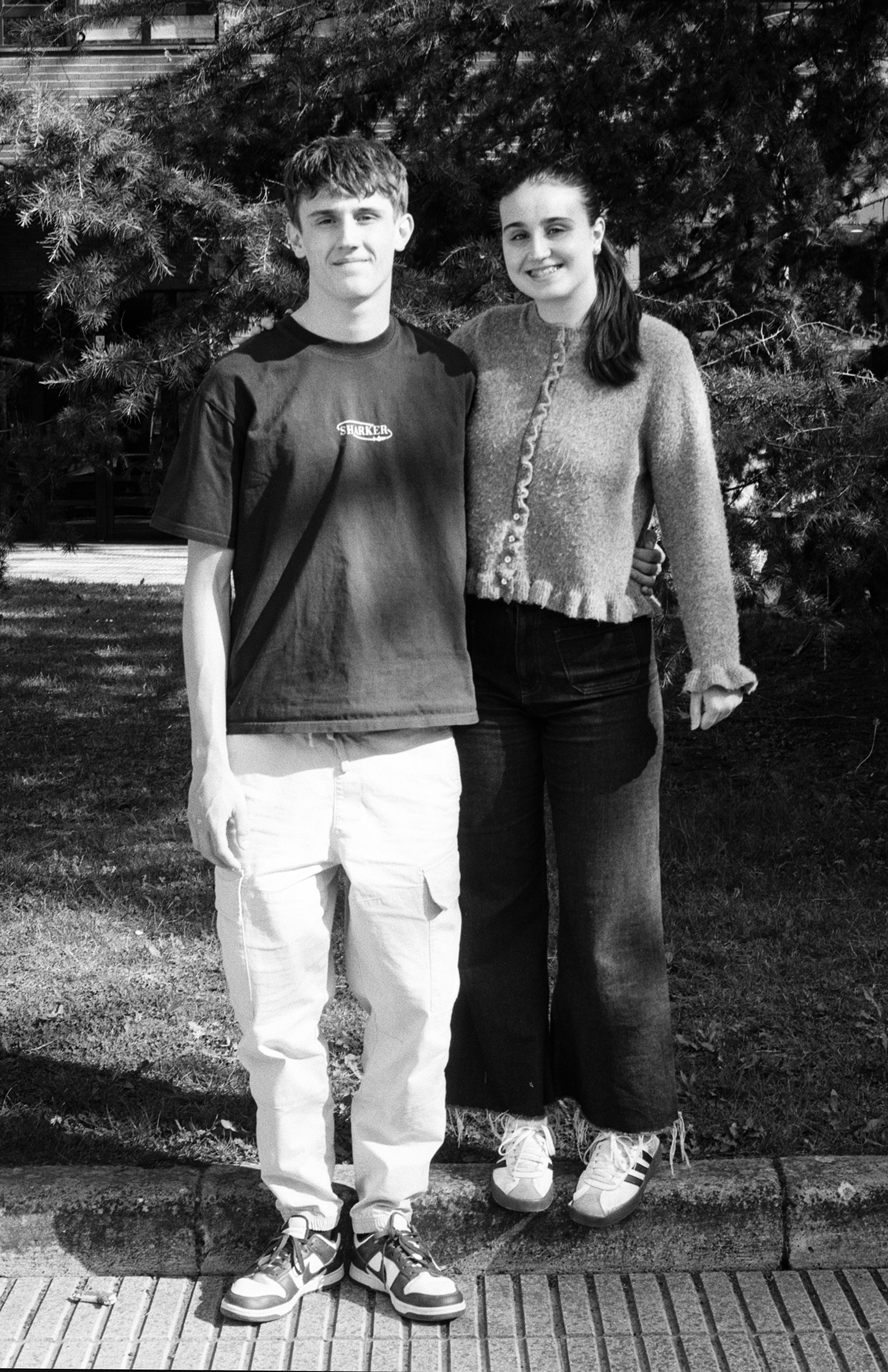 Two young people standing together outdoors against foliage background in casual clothing