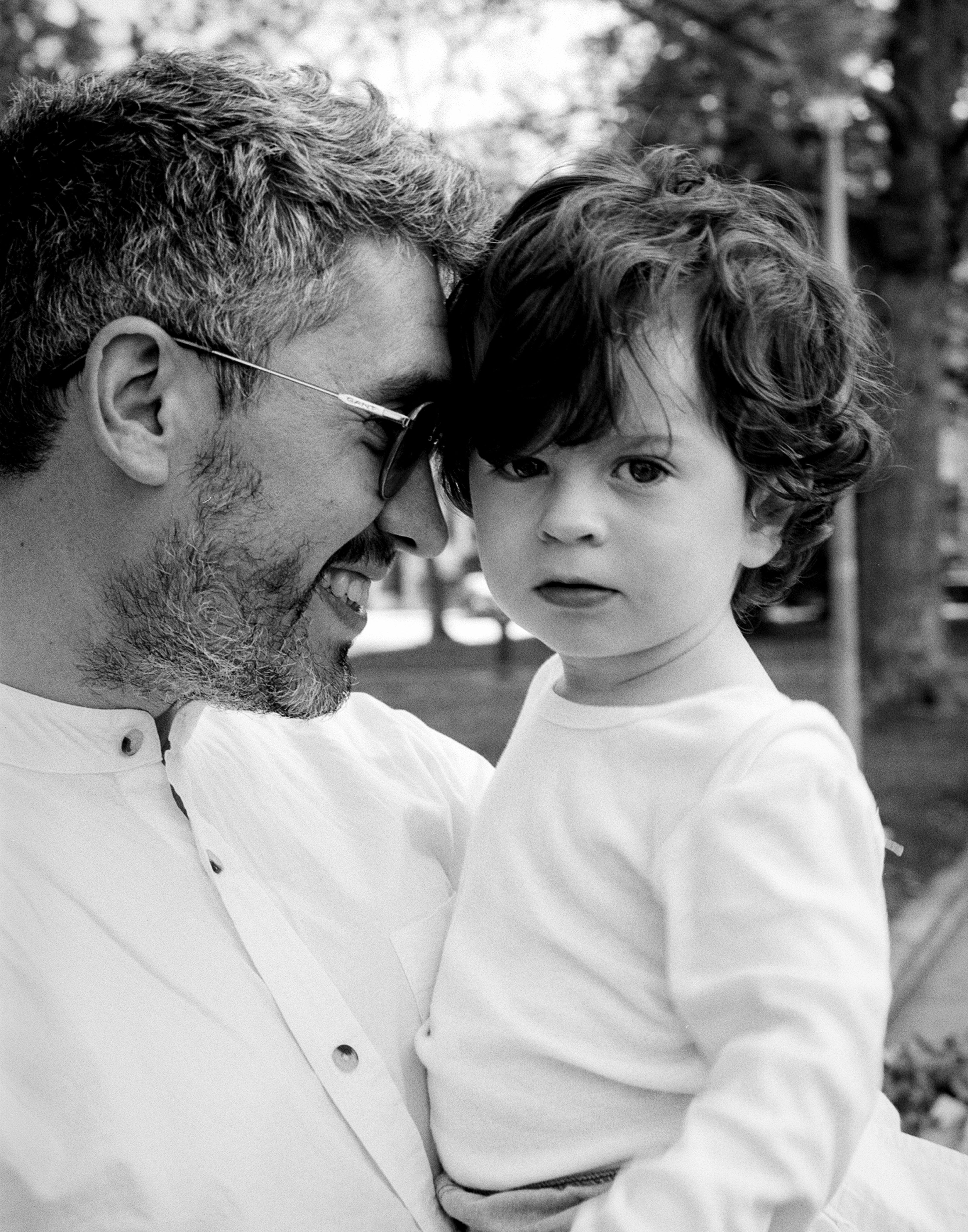 Portrait of man wearing glasses holding young child with curly hair outdoors in natural setting