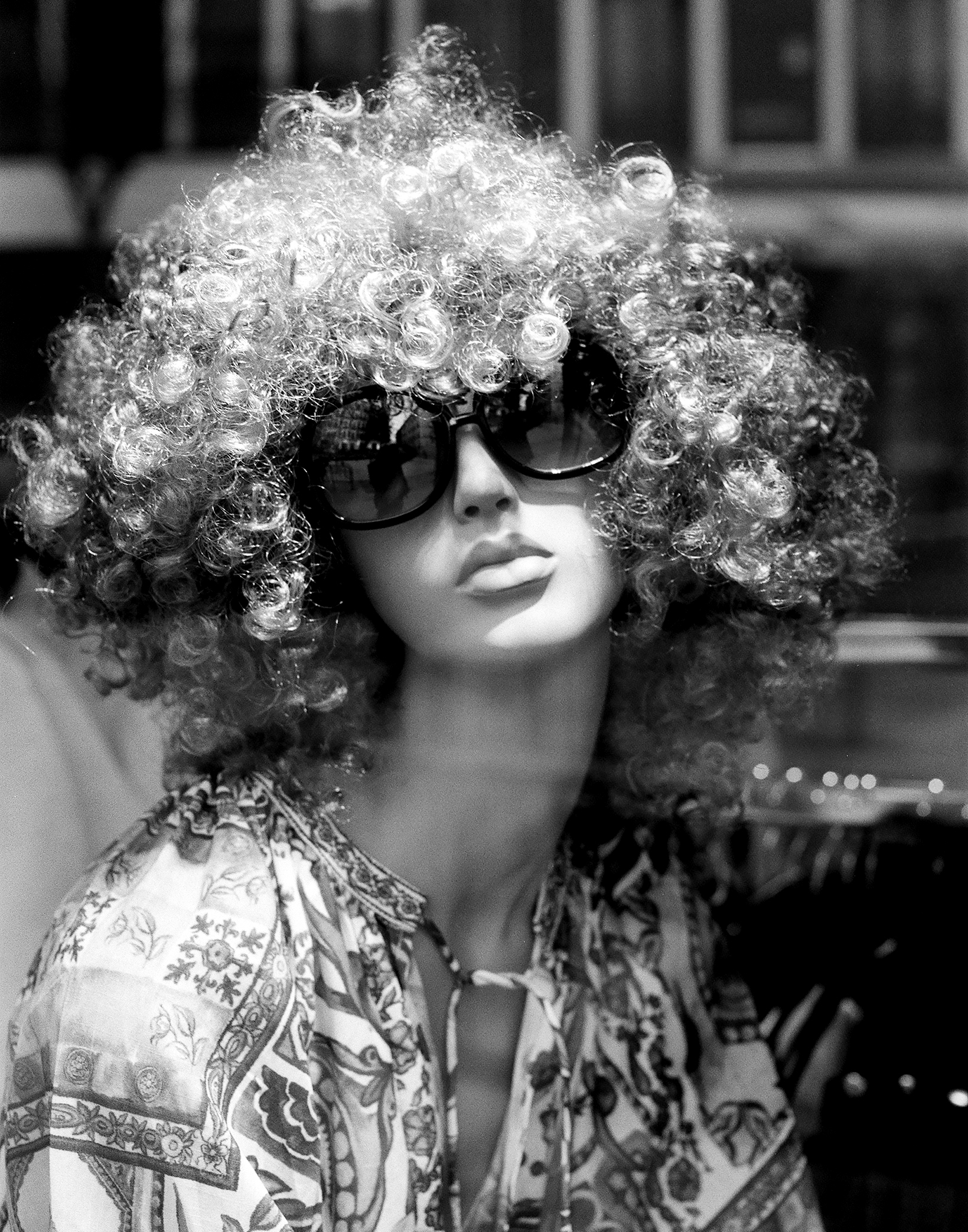 Surreal portrait of mannequin wearing large voluminous curly wig and oversized sunglasses