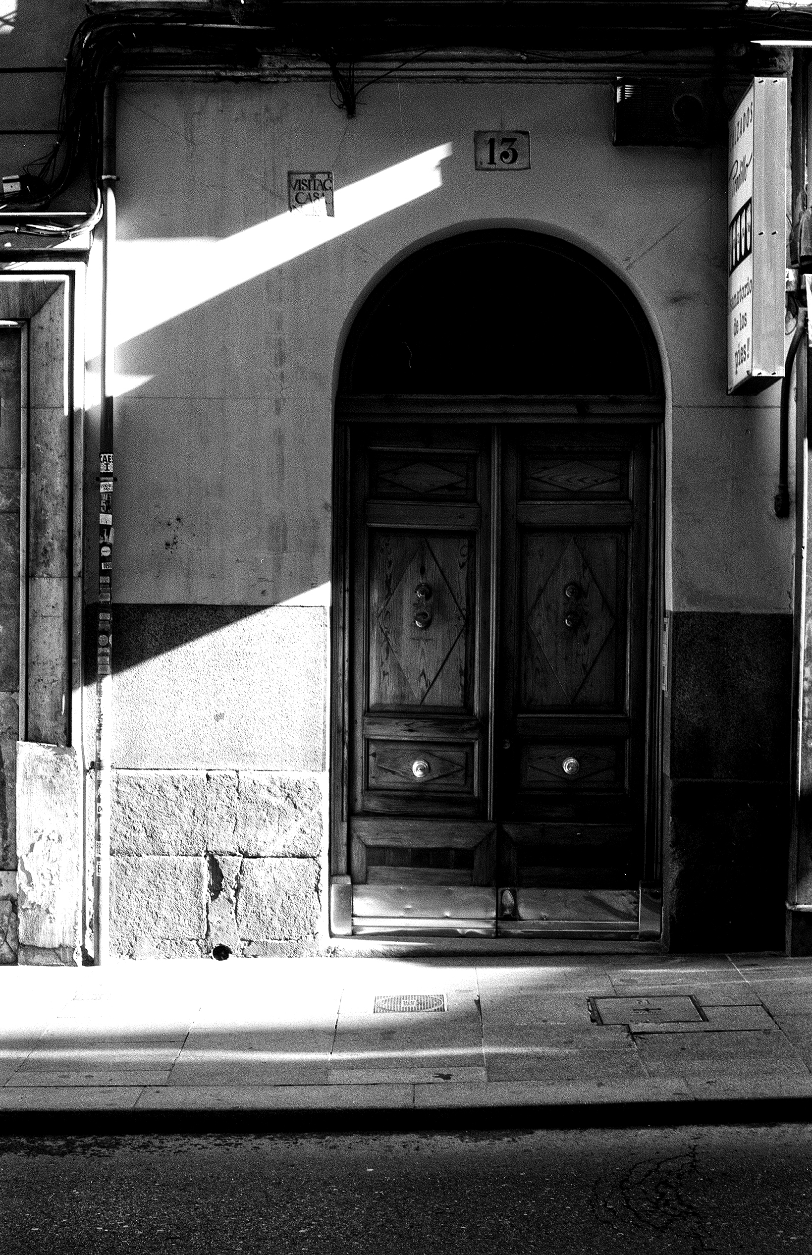 Urban doorway with arched entrance and dramatic diagonal light patterns across stone facade