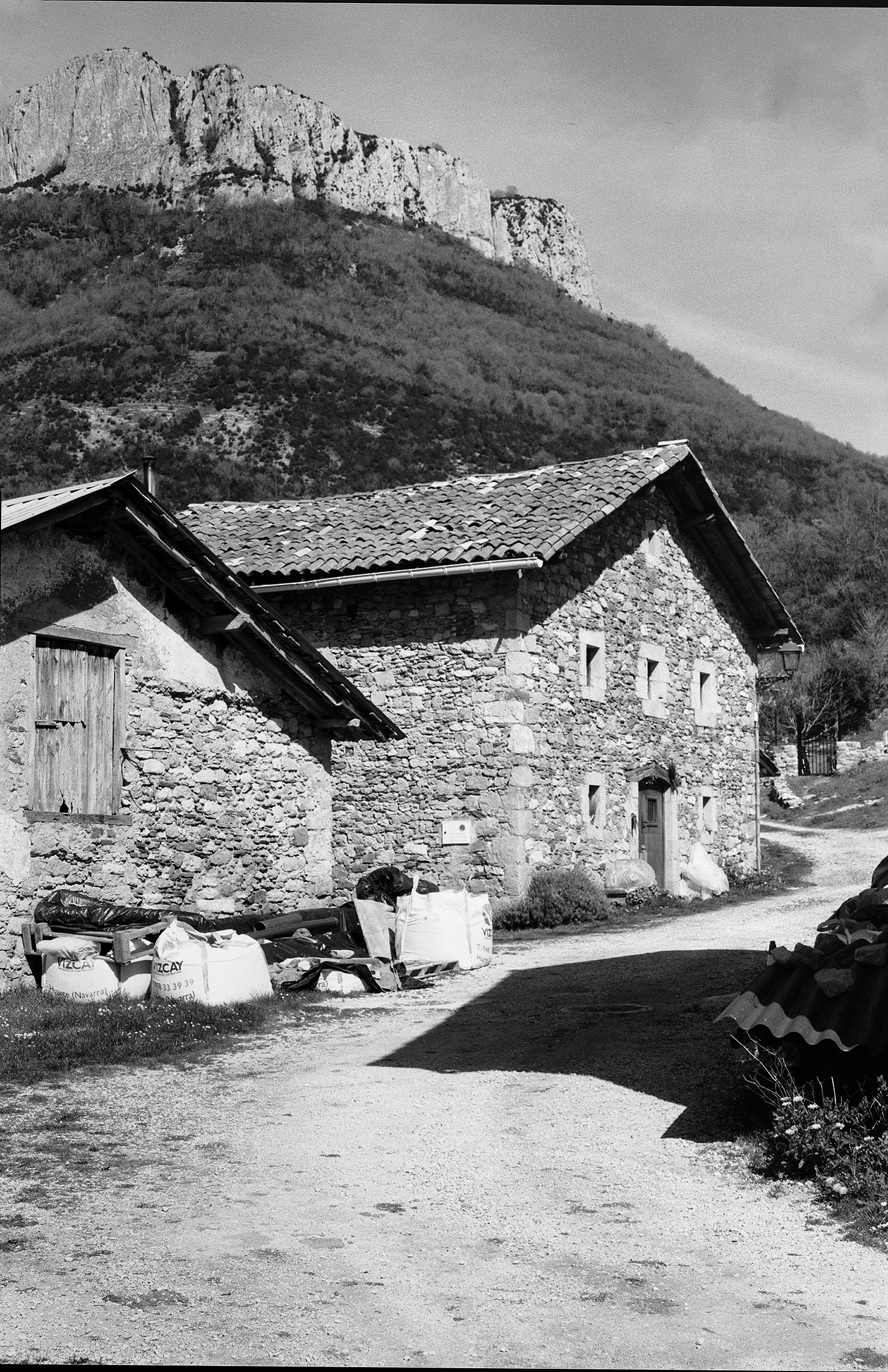 Rural stone cottage with tiled roof nestled against forested hillside landscape