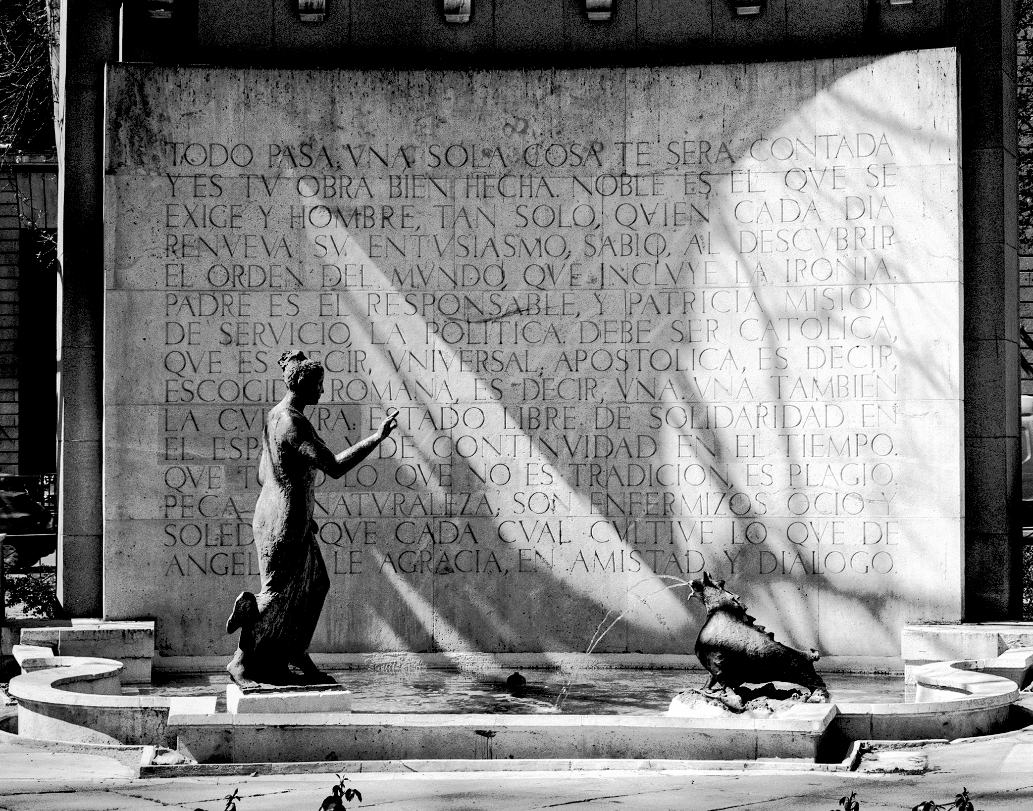 Monument with bronze sculptures and Spanish text inscription on wall backdrop