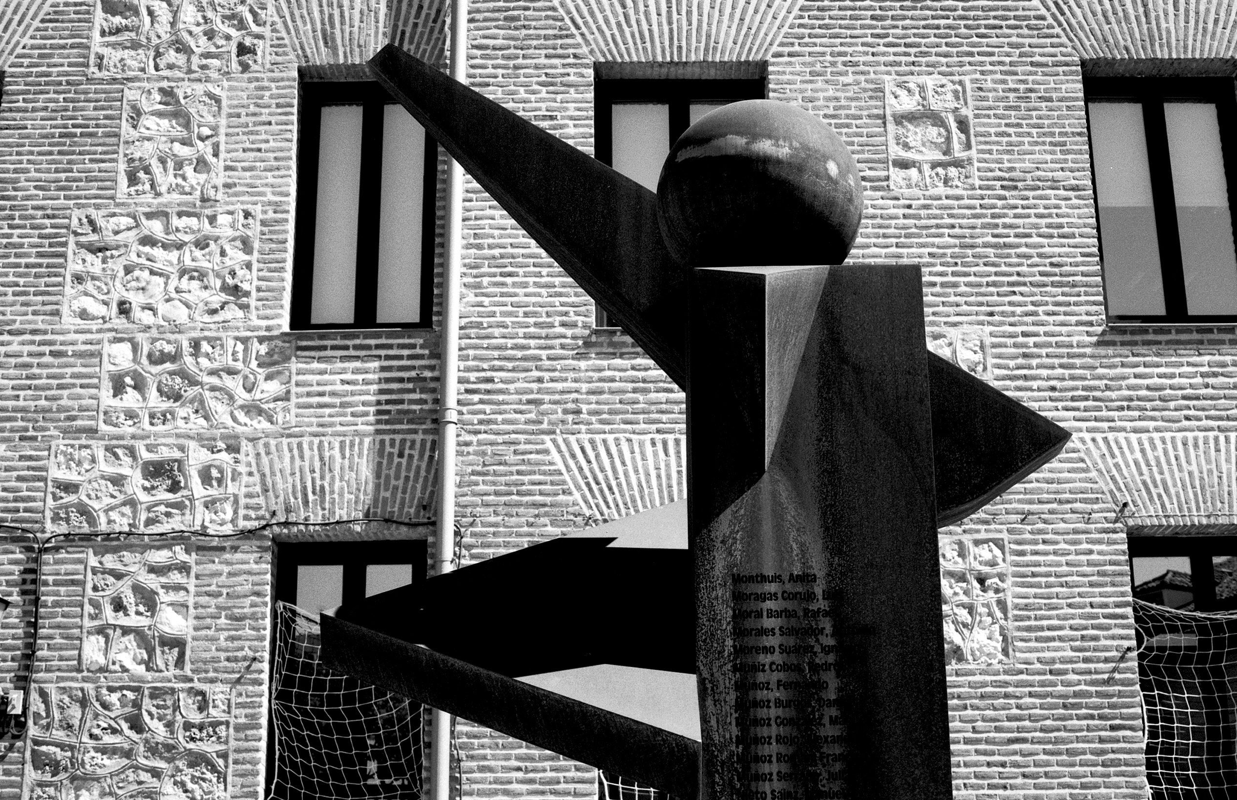 Modern geometric sculpture with curved and angular forms against brick building