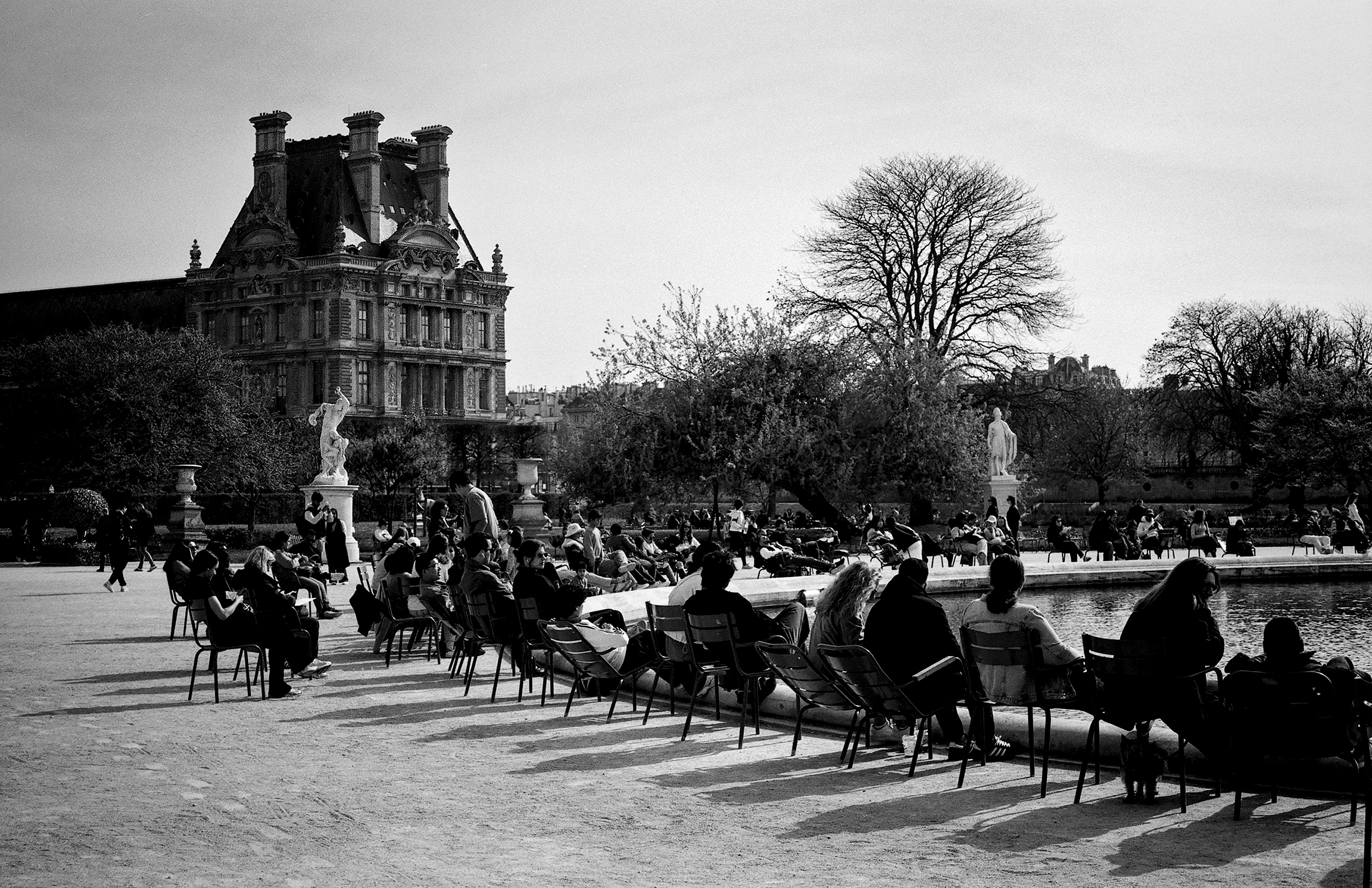 Tuileries garden with Louvre building, fountains, crowds of people seated by water
