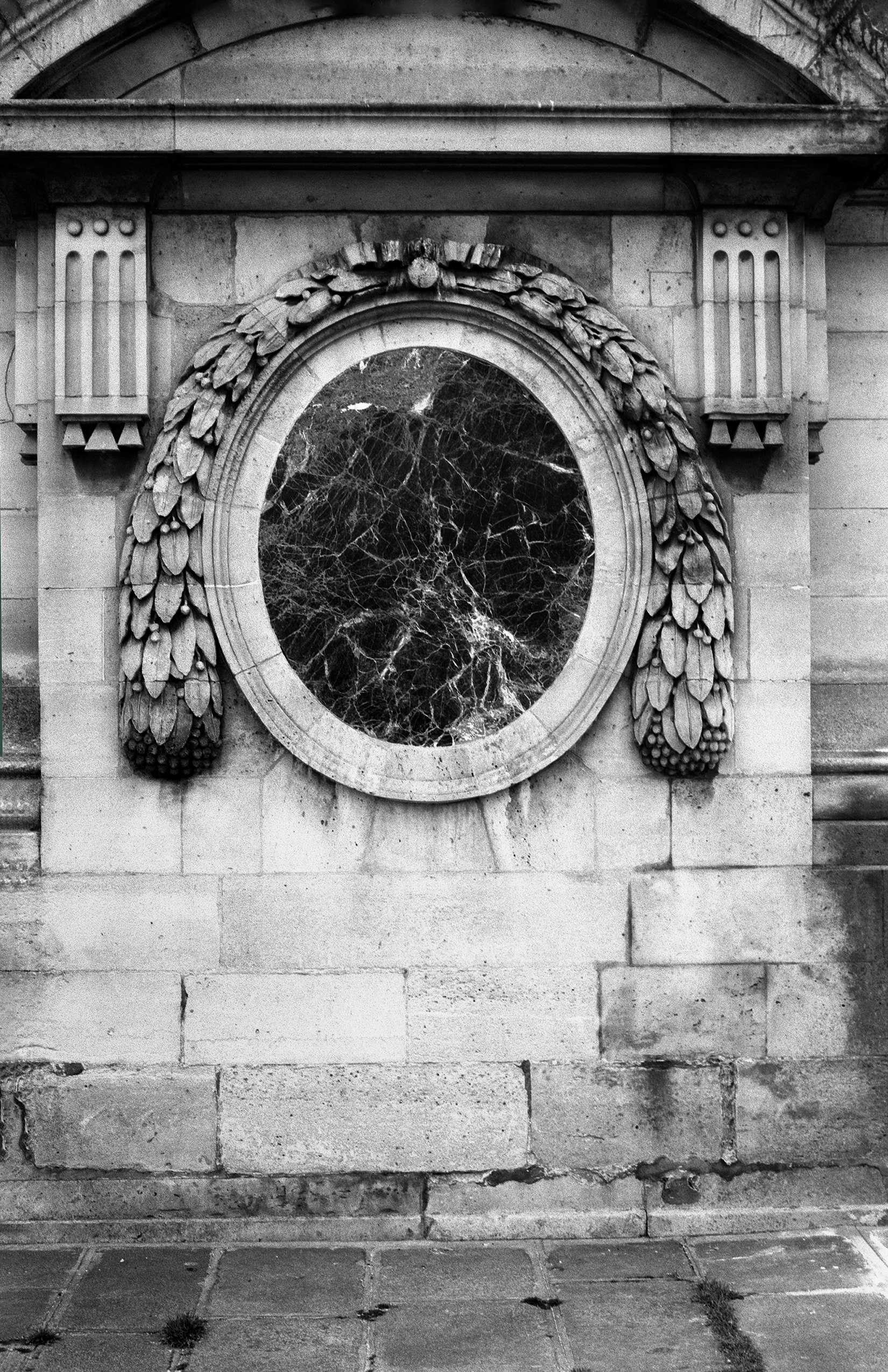 Ornate oval mirror frame with laurel wreath decoration on stone building facade