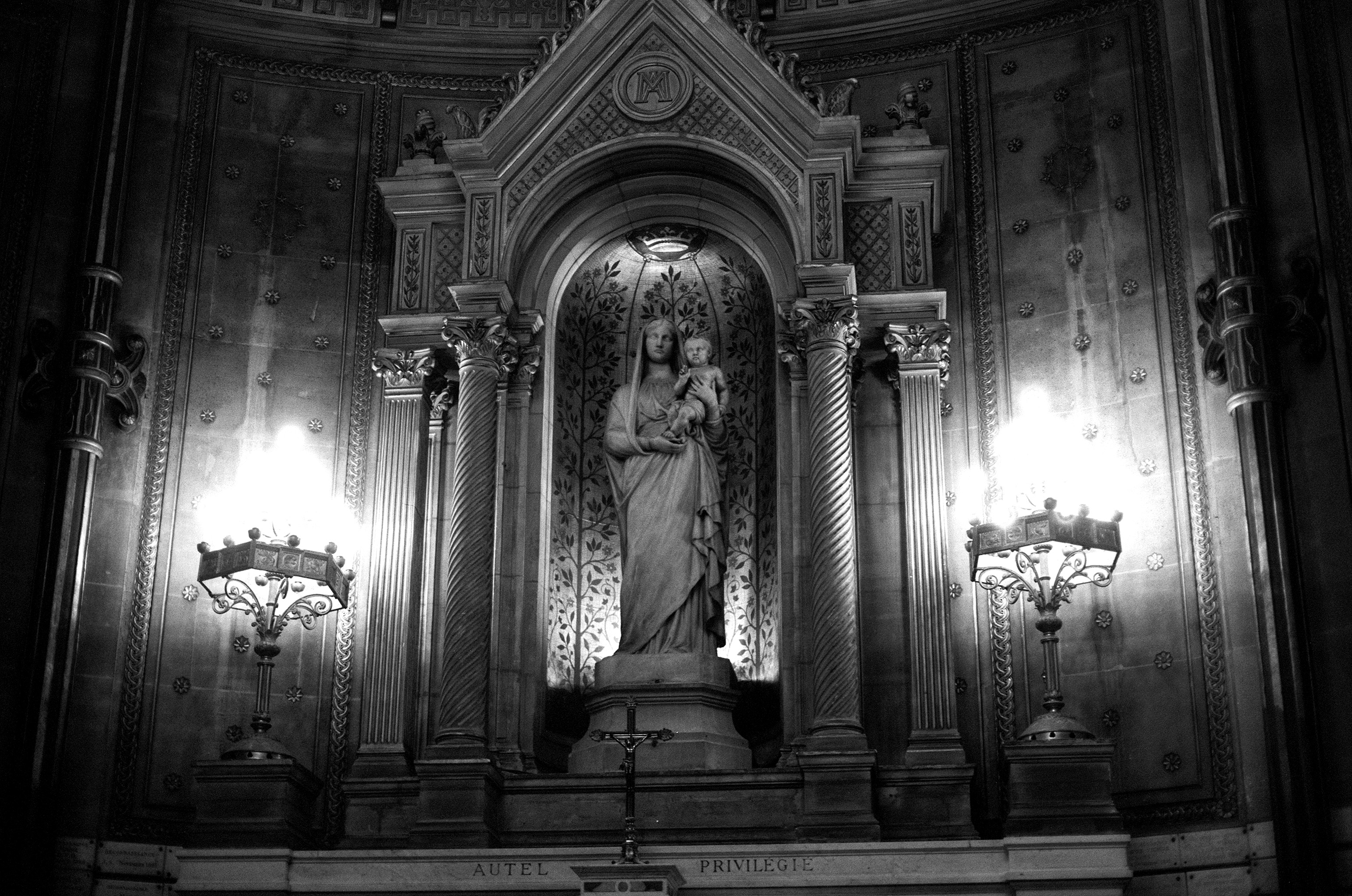 Religious altar niche with marble mother and child statue flanked by ornate Corinthian columns and candelabras