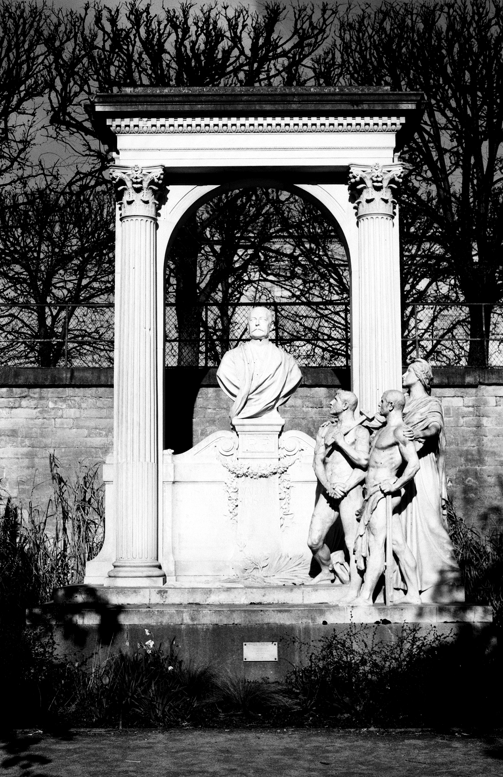 Classical marble bust in white pavilion with Corinthian columns surrounded by bare tree branches and cherub sculptures