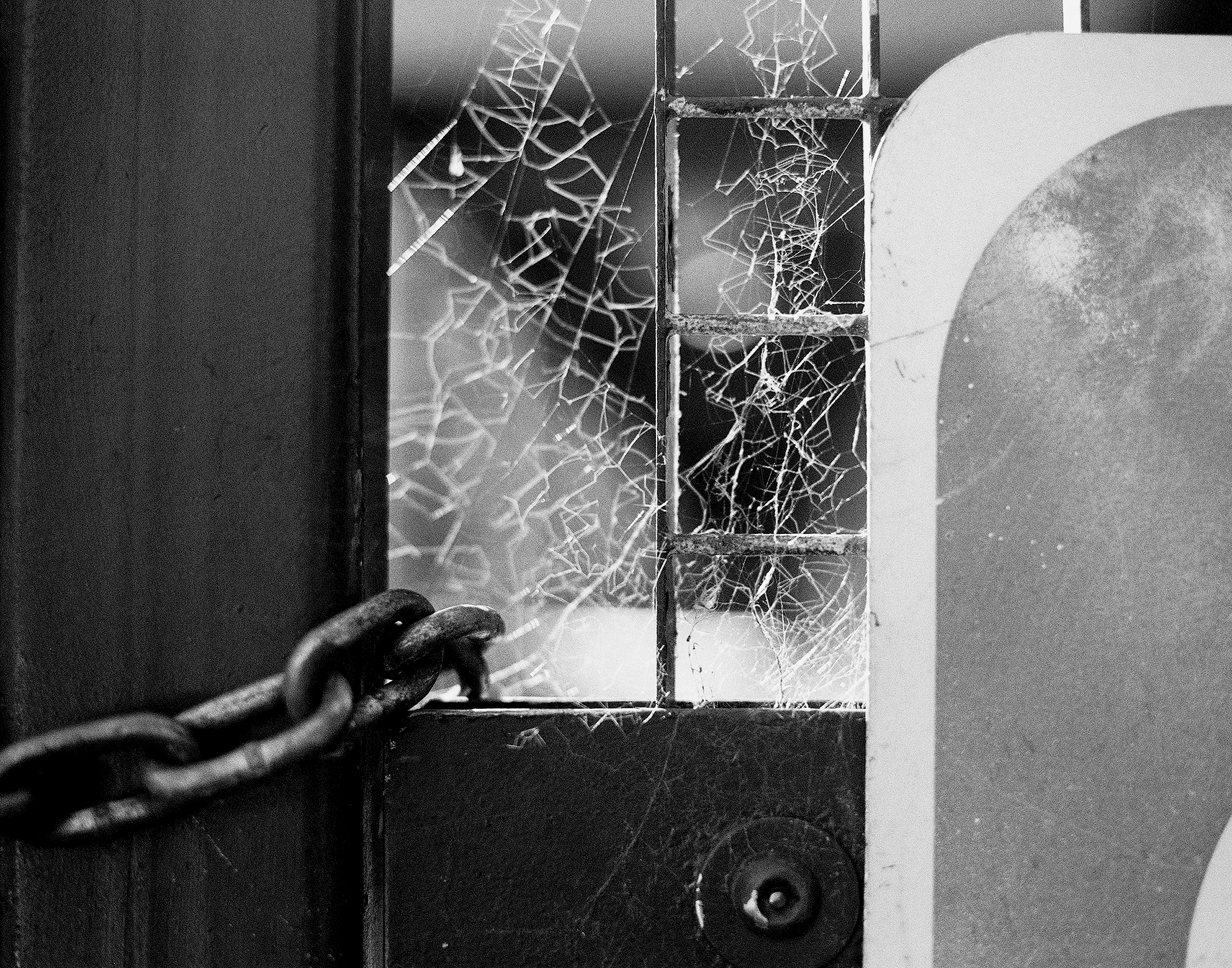 Weathered chained door with intricate spider web patterns on window panes urban decay detail