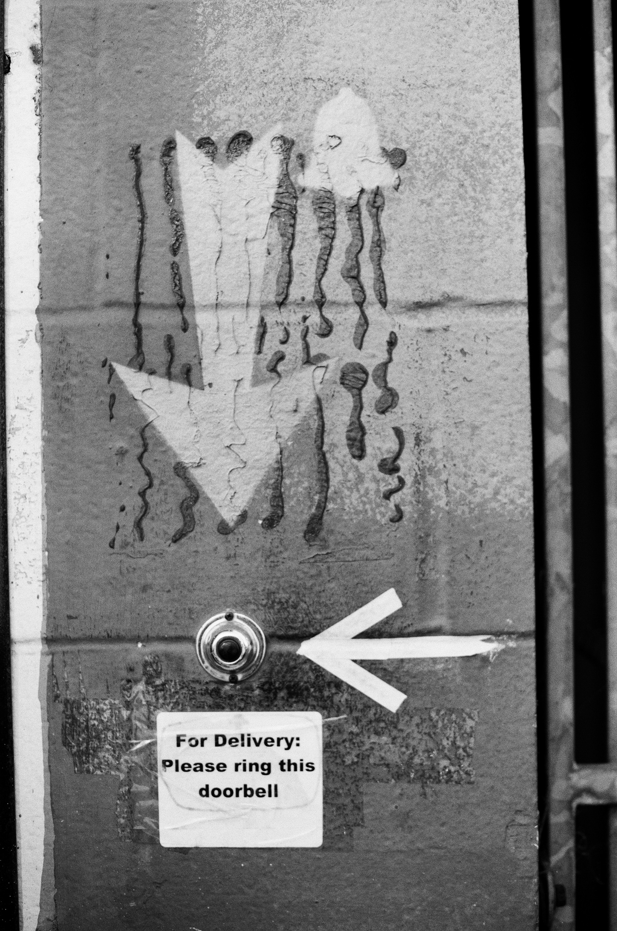 Weathered concrete wall with handwritten message and arrow pointing left with doorbell