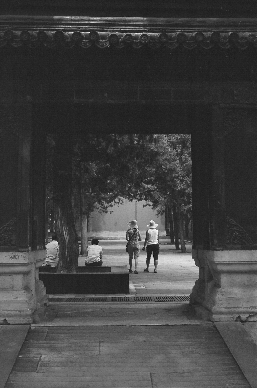 Visitors walking through traditional temple gateway with carved columns and trees