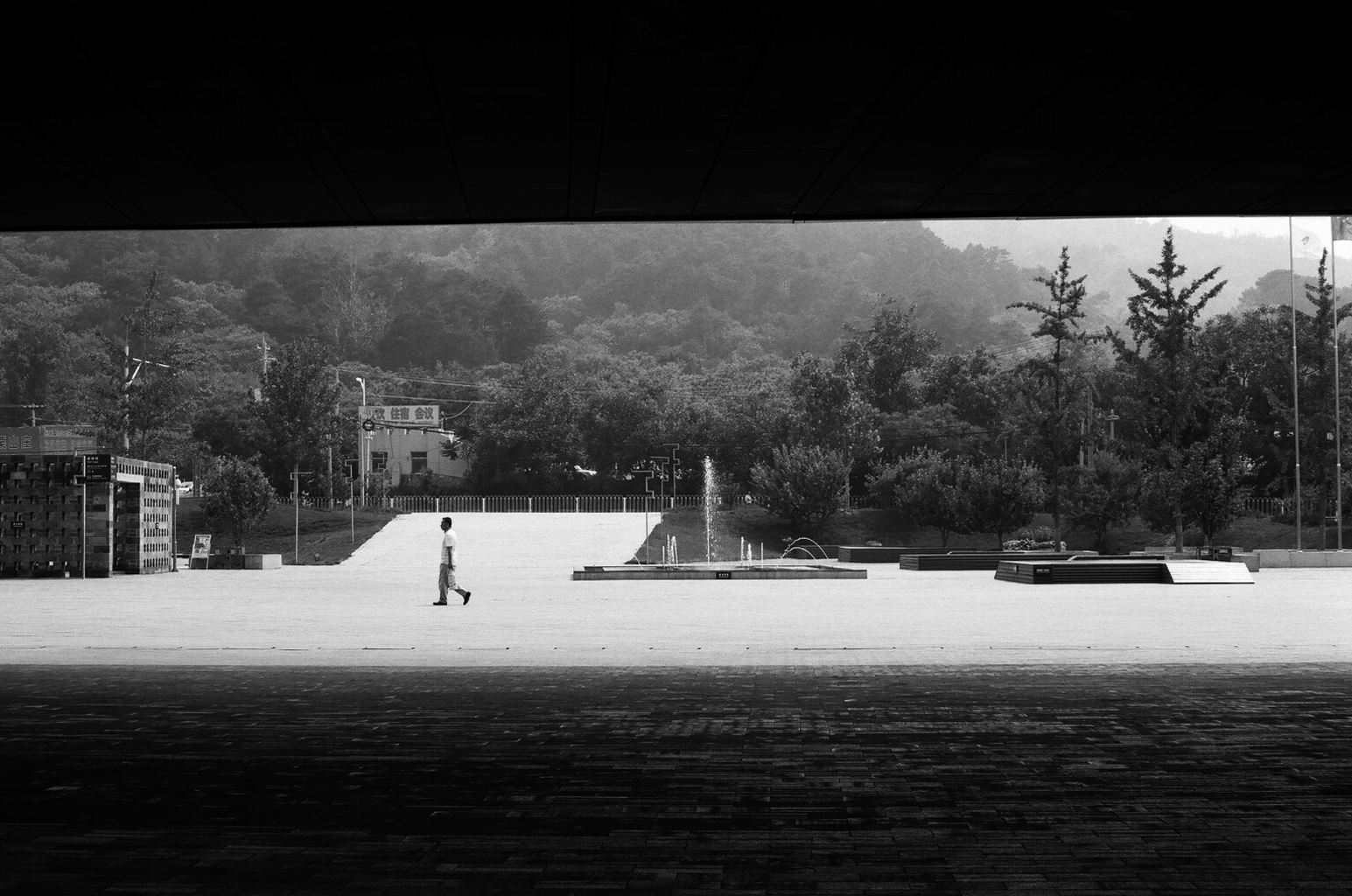 Solitary figure walking across plaza framed by dark overhang with mountains beyond