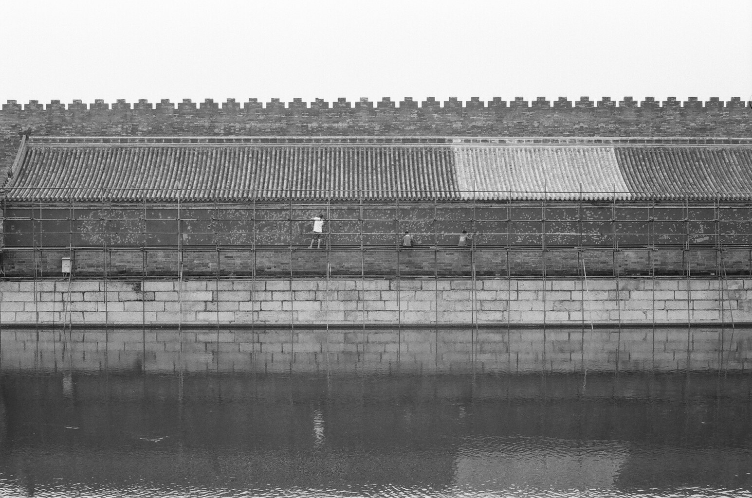 Workers on scaffolding restoring ancient fortress wall near moat water