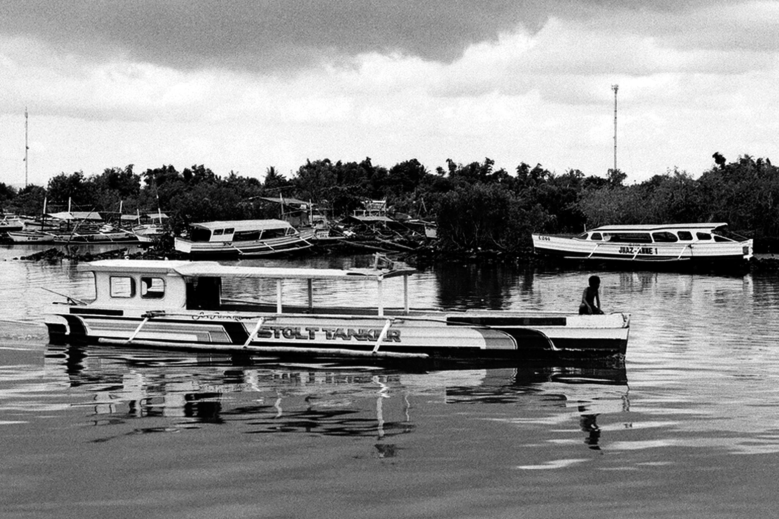 Traditional fishing boats moored in mangrove waters with palm trees and boat with person visible in background