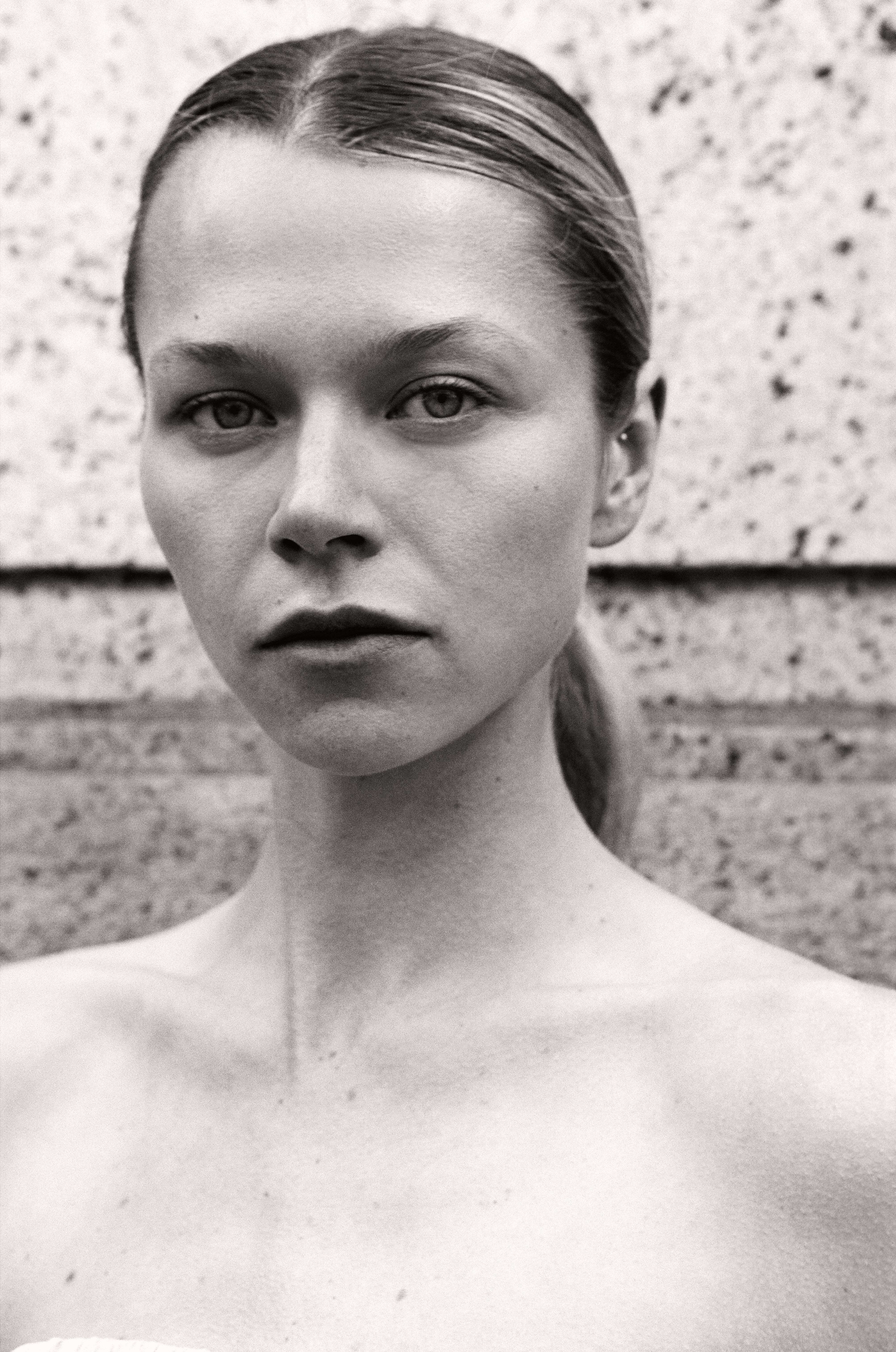 Black and white close-up beauty portrait of blonde model against speckled stone wall