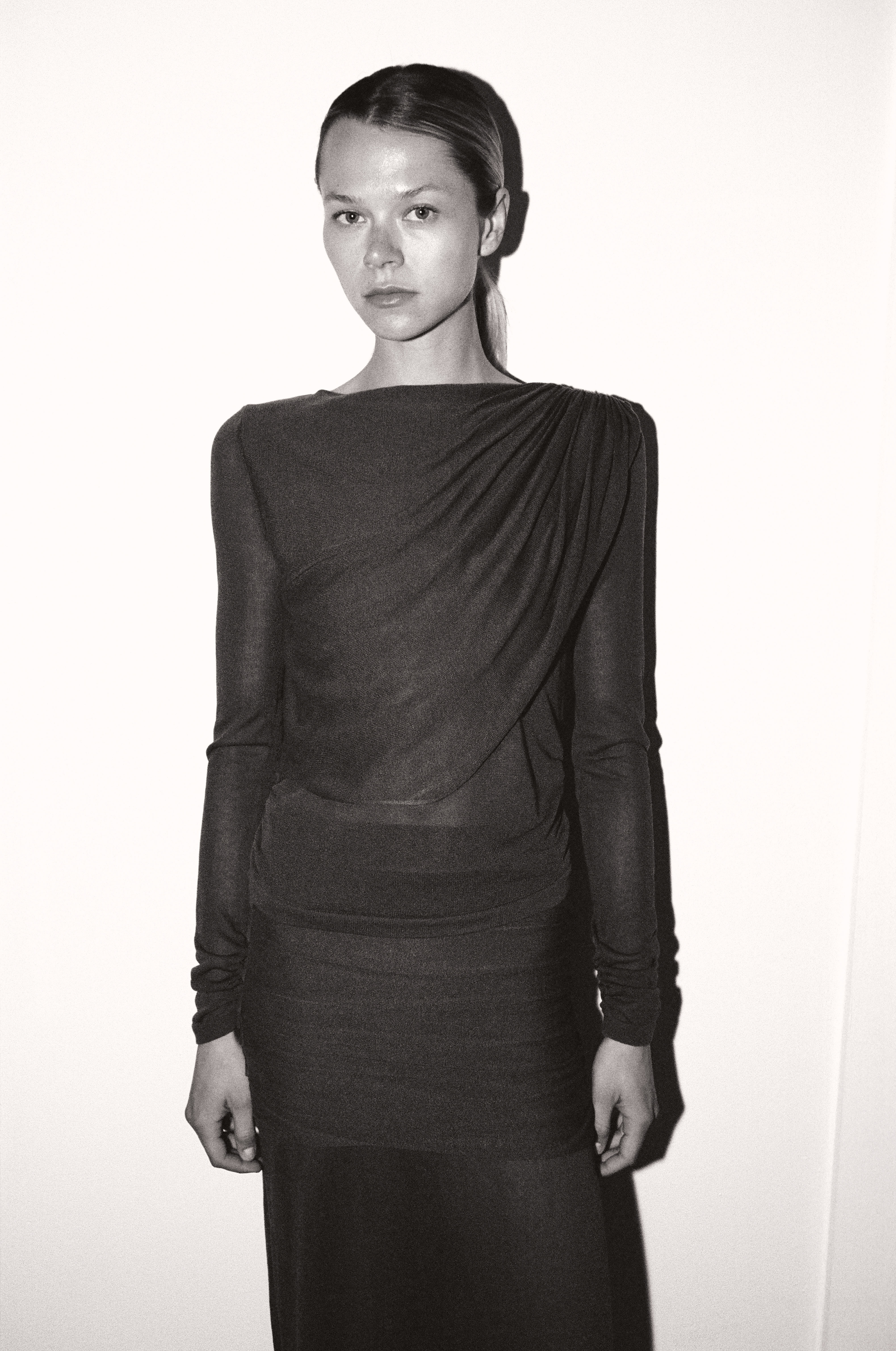 Black and white studio portrait of blonde model in draped grey jersey dress
