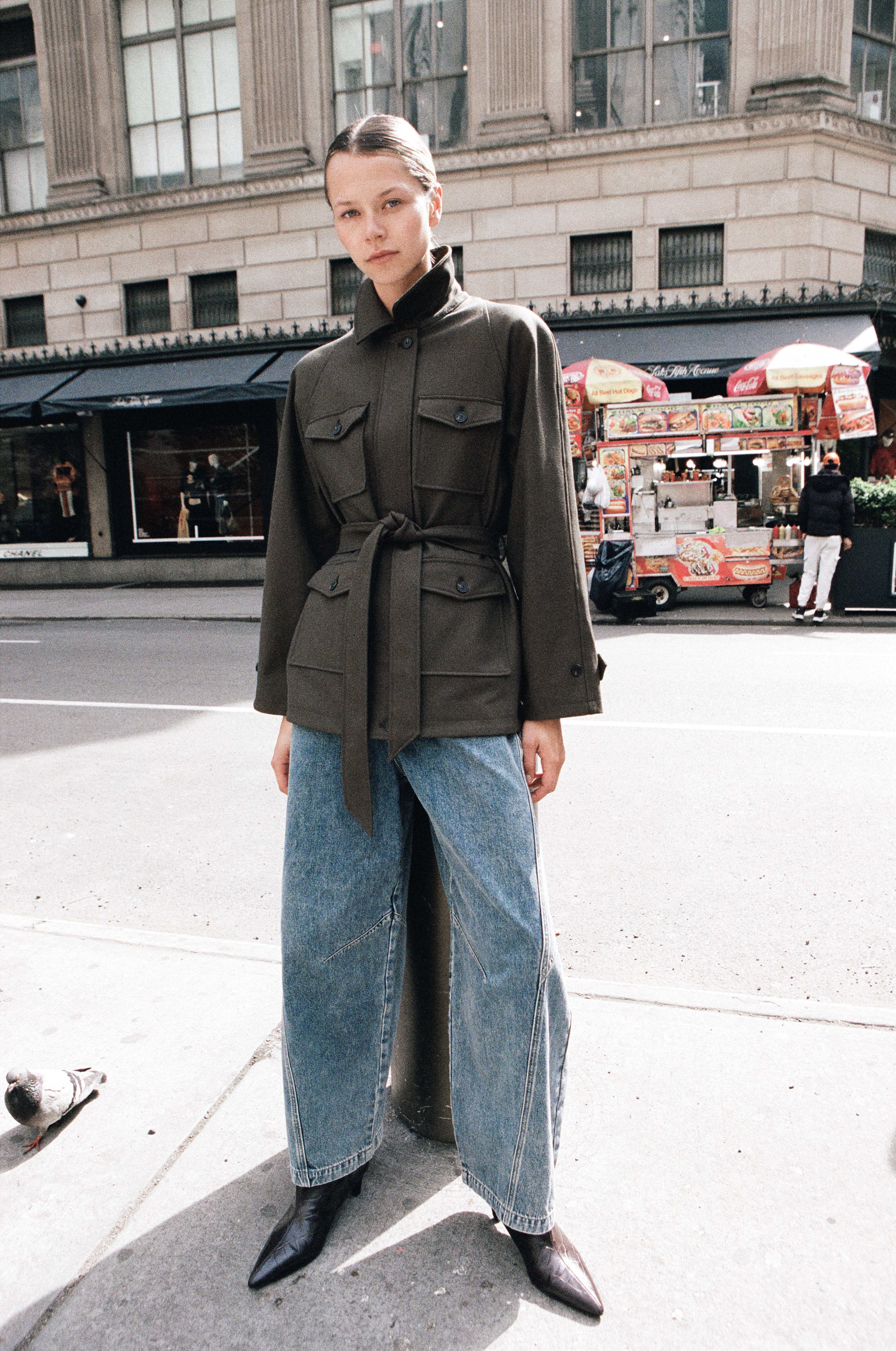 Model in olive belted military jacket and wide-leg jeans on NYC sidewalk