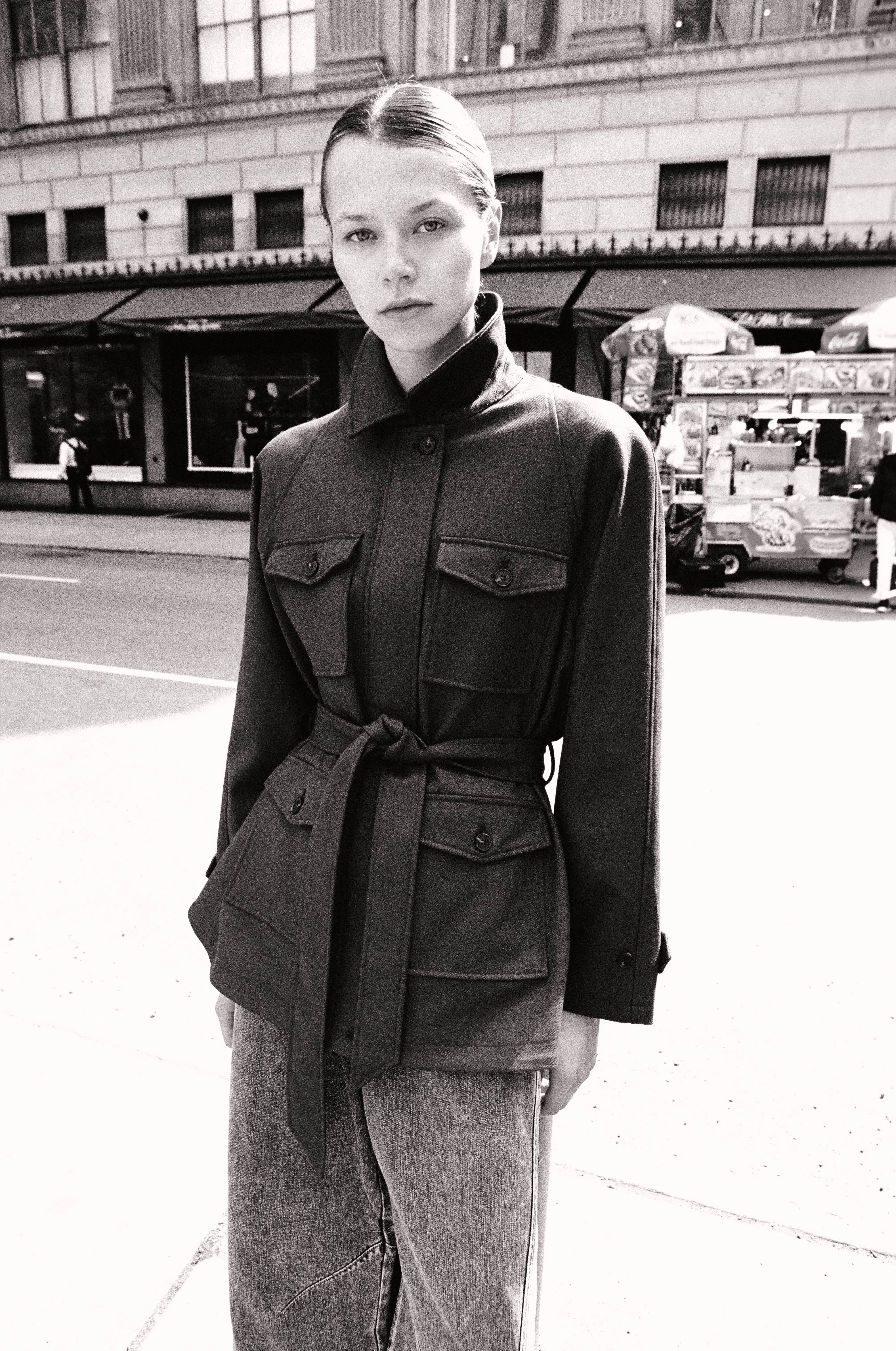 Black and white street portrait of model in olive belted military jacket in front of Saks Fifth Avenue
