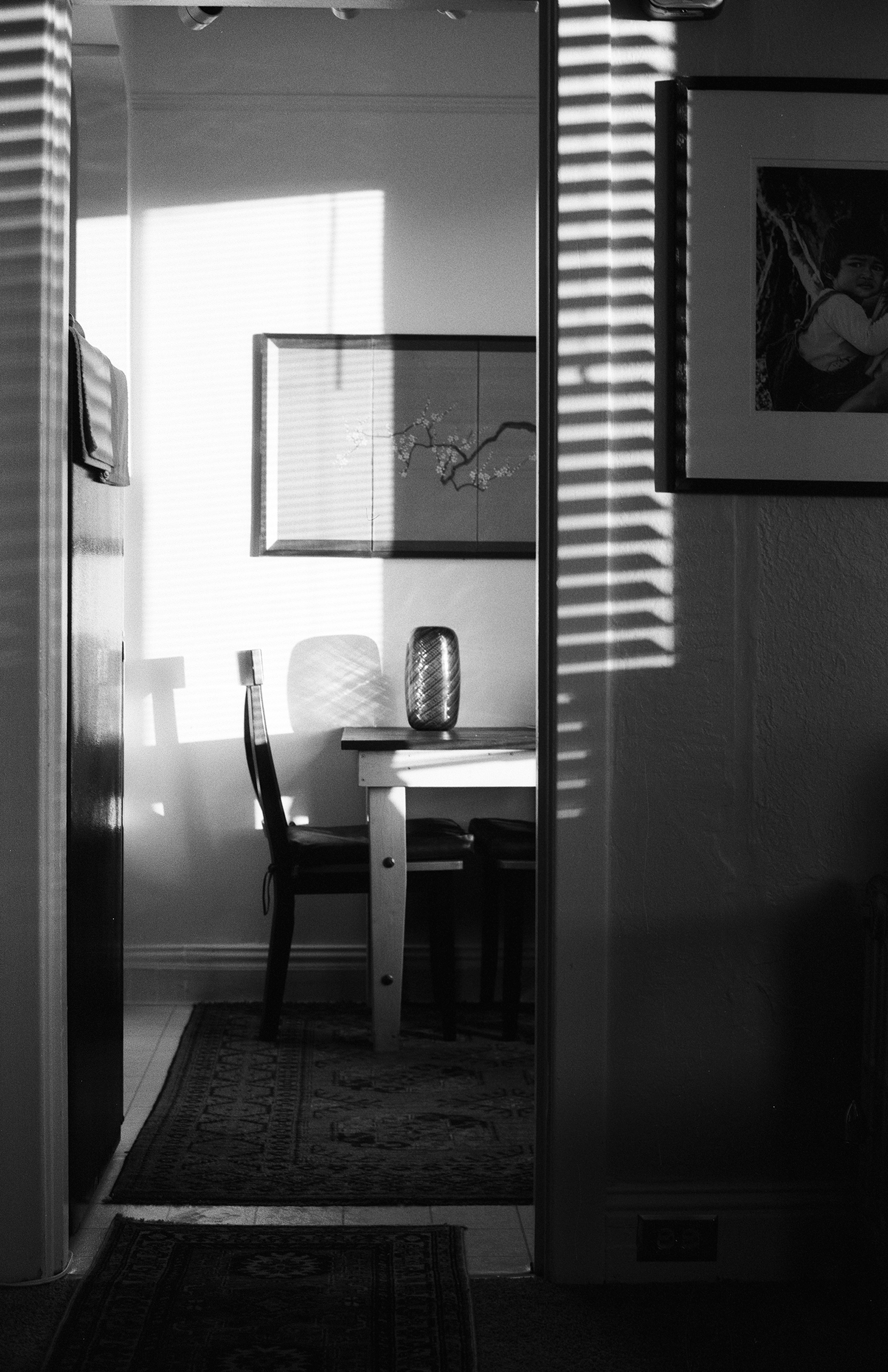 Interior room viewed through doorway showing desk with task lamp, chair, and framed artwork on wall